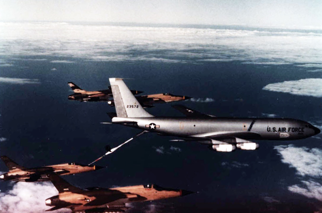 A KC-135 tanker provides fuel to a fighter jet as others fly nearby.