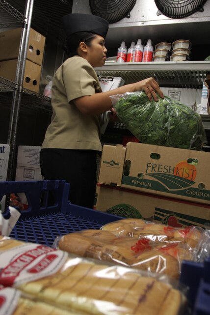 Petty Officer 3rd Class Gacayan, a preventive medicine technician in the Robert E. Bush Naval Hospital’s Preventive Medicine and Industrial Health department, checks for expired food items in a freezer locker at the hospital’s Adobe Cafe, during a routine inspection June 2.