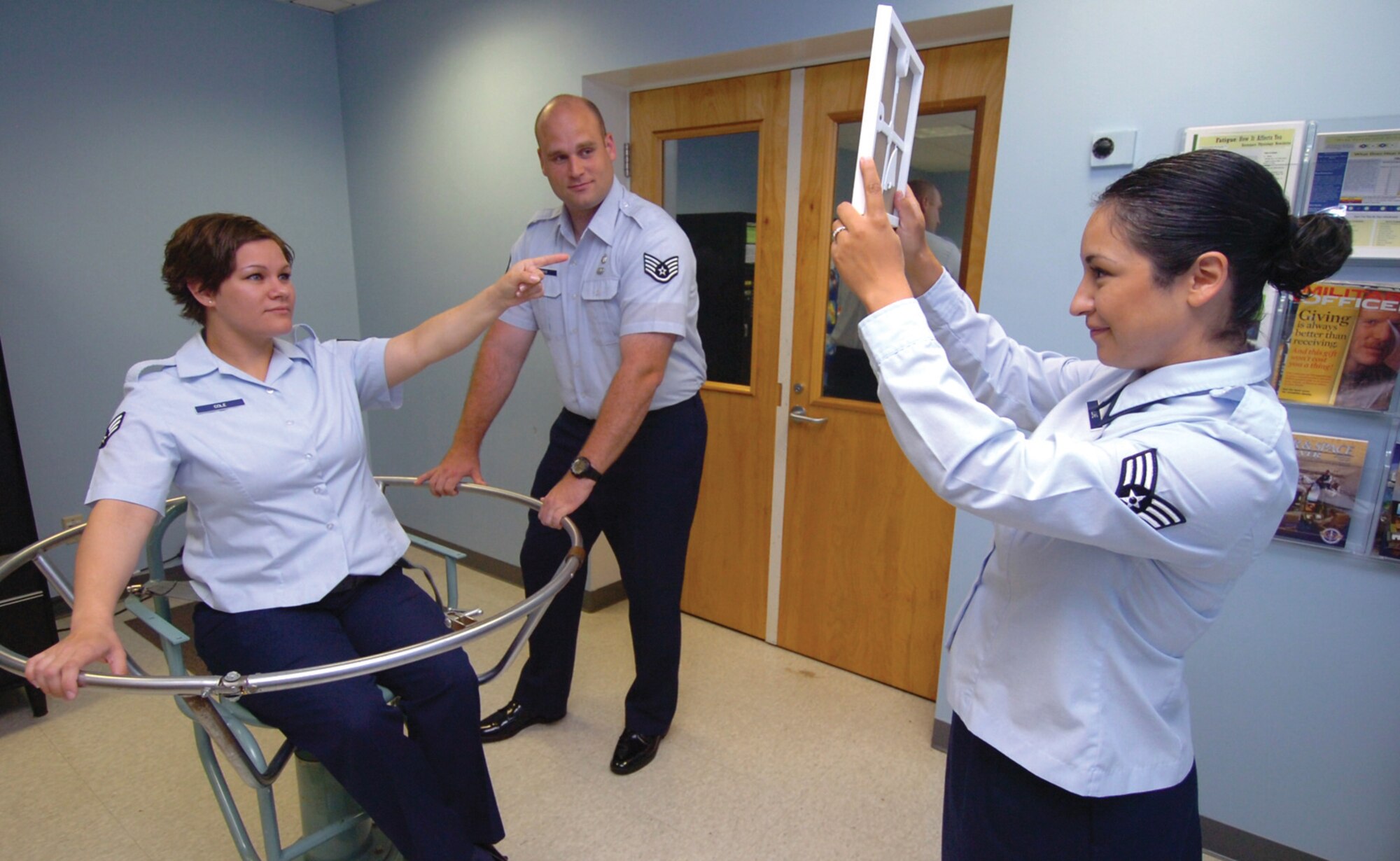 Senior Airman Rachel Cole, left, 779th Physiological Training Flight aerospace and operational physiologist, tries to point at a test board held by Senior Airman Erika Luke, 779 PTF aerospace and operational physiologist, after being spun around in a Barany Chair by Staff Sgt. J.R. Pace, 779 PTF human performance training NCO in charge. The Barany Chair is used to conduct air sickness simulation sessions for pilots, aircrew, loadmasters and flight engineers three days per week. (U.S. Air Force photo/ Bobby Jones)