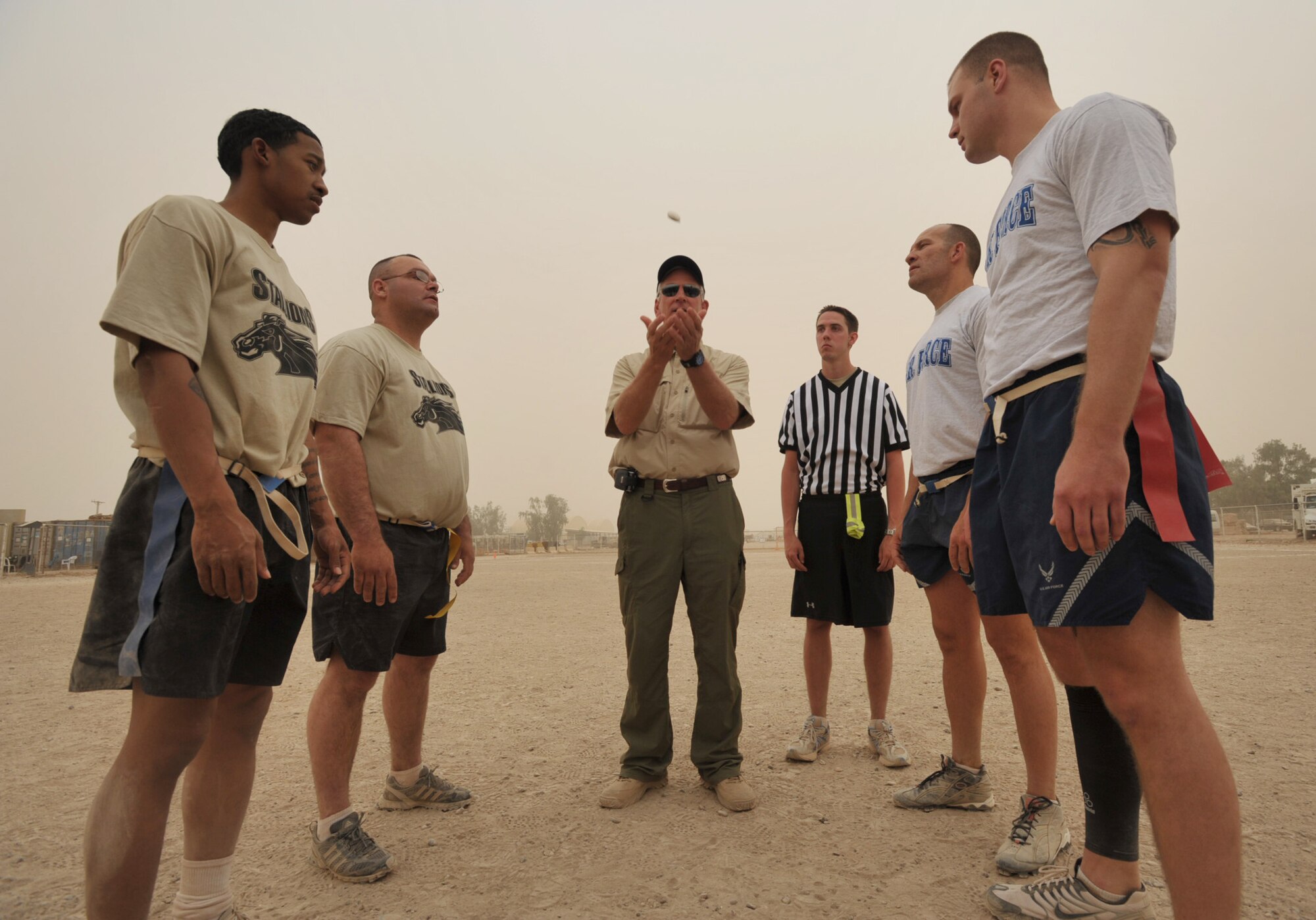 With a desert sandstorm blowing around them, two Airmen and two Soldiers join Coach Emeritus Tommy Tuberville during the opening coin toss of an Air Force-versus-Army flag football game at Joint Base Balad, Iraq, on May 31. 
Coach Tuberville and six other NCAA football coaches visited troops at the base during Coaches Tour 2009, a morale-boosting mission organized by Morale Entertainment, LLC., in association with Armed Forces Entertainment. A KC-135 Stratotanker from McConnell Air Force Base, Kan., was used to fly the coaches overseas. (U.S. Air Force photo/Tech. Sgt. Jason Schaap)