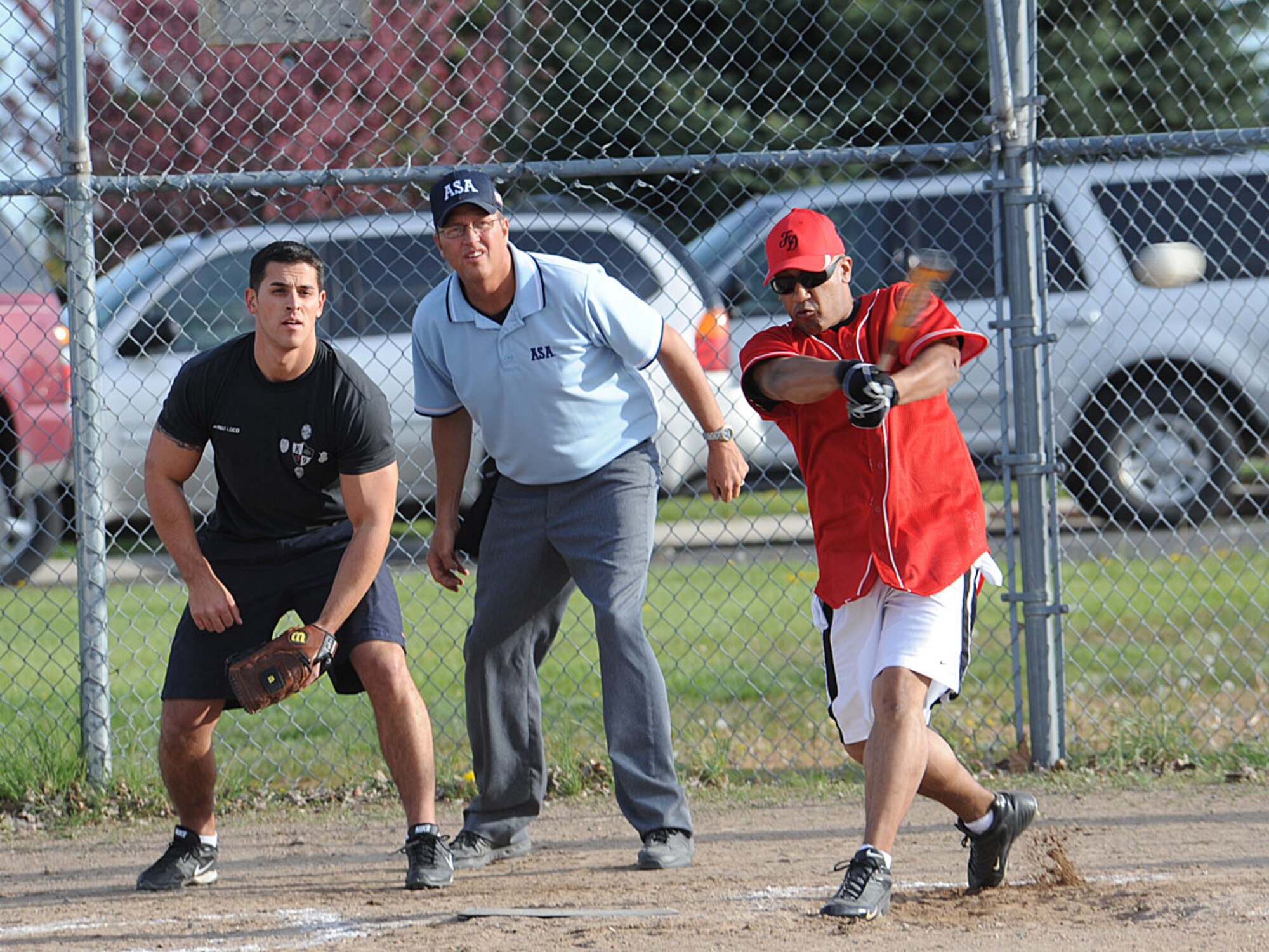 Senior Airman James Gasaway, 92nd Civil Engineer Squadron fireman, swings and hits a baseball while Staff Sgt. Jose Cadena, 92nd Security Forces military working dog handler, and Master Sgt. Richard Van Sickle, 336th Training Squadron information management functional, watch the ball make its way out into the outfield here May 16. The 92nd Security Forces Squadron defeated the 92nd Civil Engineer Squadron fire department in the first ever Battle of the Badges softball game coinciding with National Police Week. (U.S. Air Force photo / Staff Sgt. JT May III)