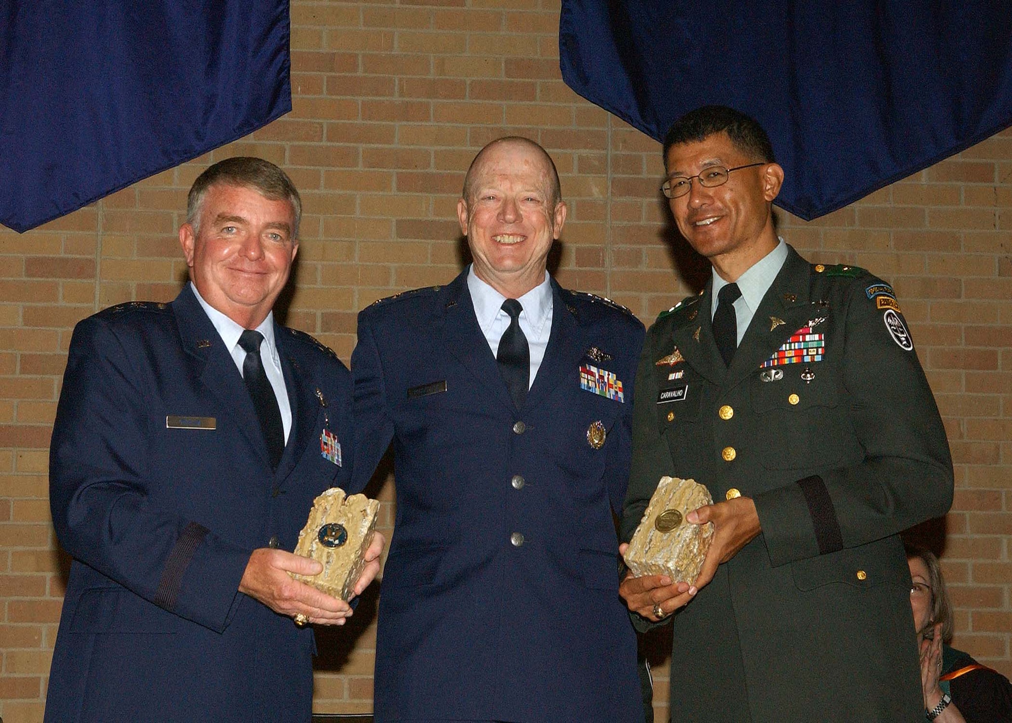 Maj. Gen. Tom Travis (left), 59th Medical Wing commander, and Army Brig. Gen. Joseph Caravalho, Jr. (right), Brooke Army Medical Center commander, present commemorative Texas bookends to Lt. Gen. James Roudebush, the Air Force surgeon general, during the San Antonio Uniformed Services Health Education Consortium awards and graduation ceremony June 5 at the University of Texas Health Science Center at San Antonio. During the graduation portion of the ceremony, 243 graduates from 36 graduate medical education programs and 50 graduates from 13 allied health care programs received diplomas. (U.S. Air Force photo/Alan Boedeker) 