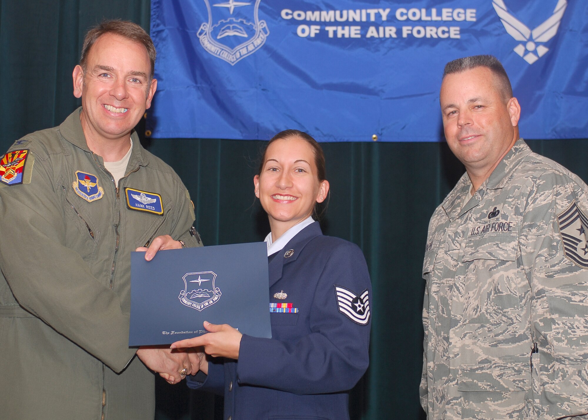 Col. Hank Reed, 56th Fighter Wing vice commander, presents Tech. Sgt. Nicole Emler, 944th Services Flight, with her Community College of the Air Force degree as Chief Master Sgt. Randall Raper, 56th Fighter Wing command chief, looks on. Sergeant Emler received her CCAF during the Luke AFB graduation May 21. (Courtesy photo)