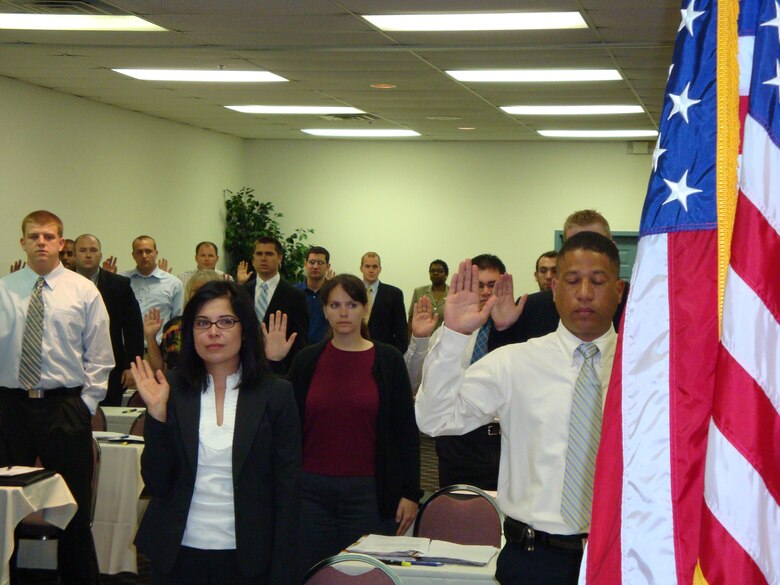 A group of more than 30 civilians raise their hands as part of the process to officially become federal employees.  After a period of training, the new hires, most with advanced degrees, will become contracting specialists working for various contracting organizations here. (Air Force photo by Ron Fry) 