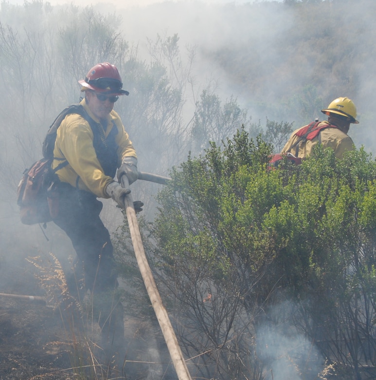 VANDENBERG AIR FORCE BASE, Calif. – Vandenberg firefighters, Vince Culliver and Captain Bill Burch, stretch their hoses through thick brush while attempting to put out the fire at the Lompoc Penitentiary Shooting Range near Vandenberg June 11.  Due to the fact that California is in the middle of its fire season, a large amount of resources responded from Vandenberg, Lompoc and Santa Barbara County to extinguish the flames. (Photo by Andrew Klein)