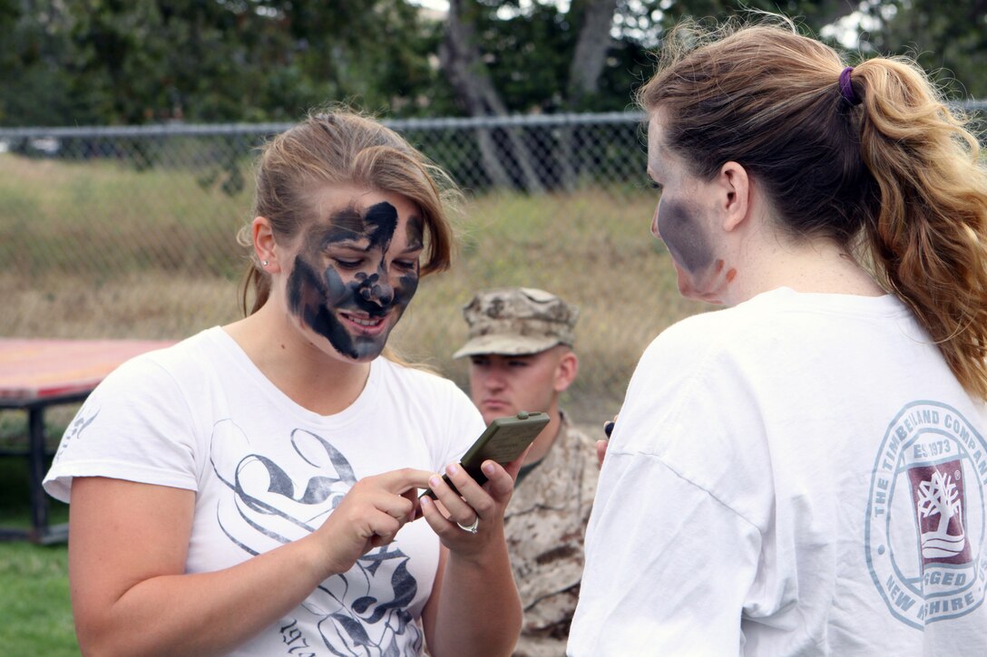 Military spouse, Alana Herring, applies camouflage paint to a fellow spouse during the School of Infantry West Jane Wayne Day, June 13.