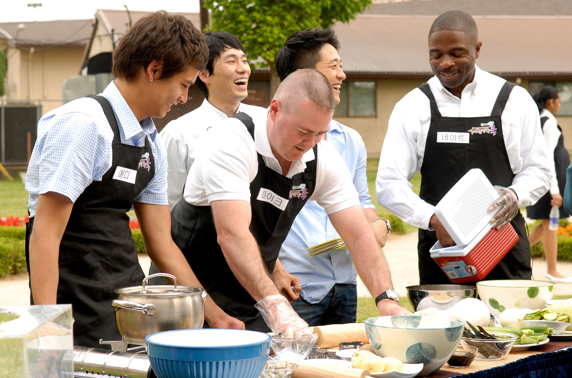 From left to right, Eddie Timm watches as Tech. Sgt. Michael Tipton, uses a roller to fl atten out dough as Senior Master Sgt. Nathan Stephens reaches for ingredients during the fi lming of Delicious Korea (Dae Han Min Guk), June 8. The South Korean television studio filmed Team Osan members as they prepared traditional South Korean meals. This is the first time United States military members have been in the show. Mr. Timm works for the 51st Services Squadron, Sergeant Tipton is a member of the 51st Mission Support Squadron and Sergeant Stephens is a member of the 51st Maintenance Operations Squadron.(U.S. Air Force photo/Senior Airman Stephenie Wade).