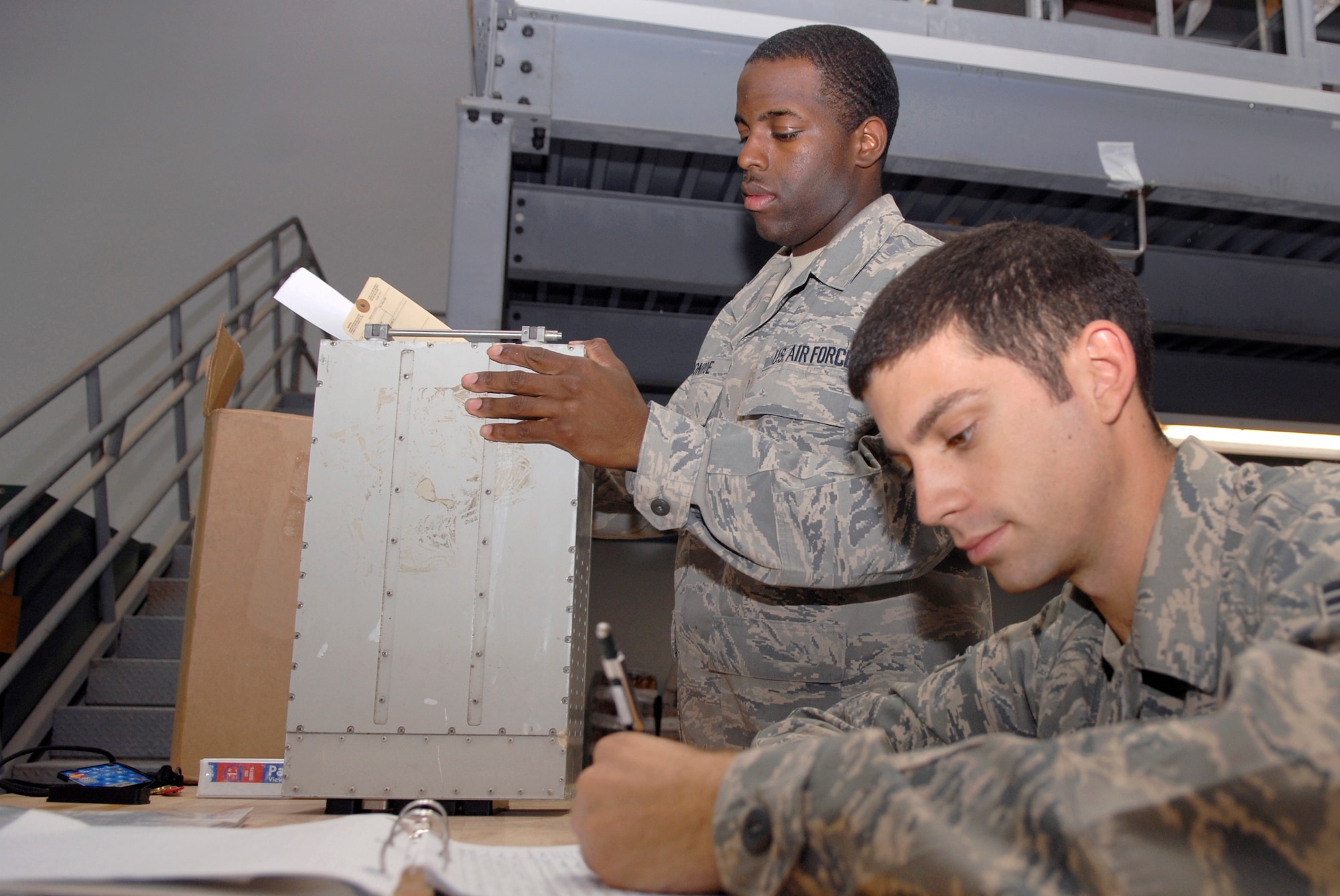 Airman 1st Class Derrick Monroe, 379th Expeditionary Aircraft Maintenance Squadron combat oriented supply organization (COSO) journeyman, checks in a bad part for maintenance from Senior Airman Michael Martin, a 379th Expeditionary Maintenance Squadron B1-B avionics technician, while he fills out the paperwork for it, June 9, 2009, at an undisclosed location in Southwest Asia.  COSO personnel manage the supply of parts and assist maintenance technicians in researching and locating parts they need to perform their mission.  Airman Monroe hails from Albany, Ga.  Airman Martin hails from Rehoboth, Del.  Both are deployed from Dyess Air Force Base, Texas, in support of Operations Iraqi and Enduring Freedom and Combined Joint Task Force - Horn of Africa.  (U.S. Air Force photo/Senior Airman Andrew Satran/released)