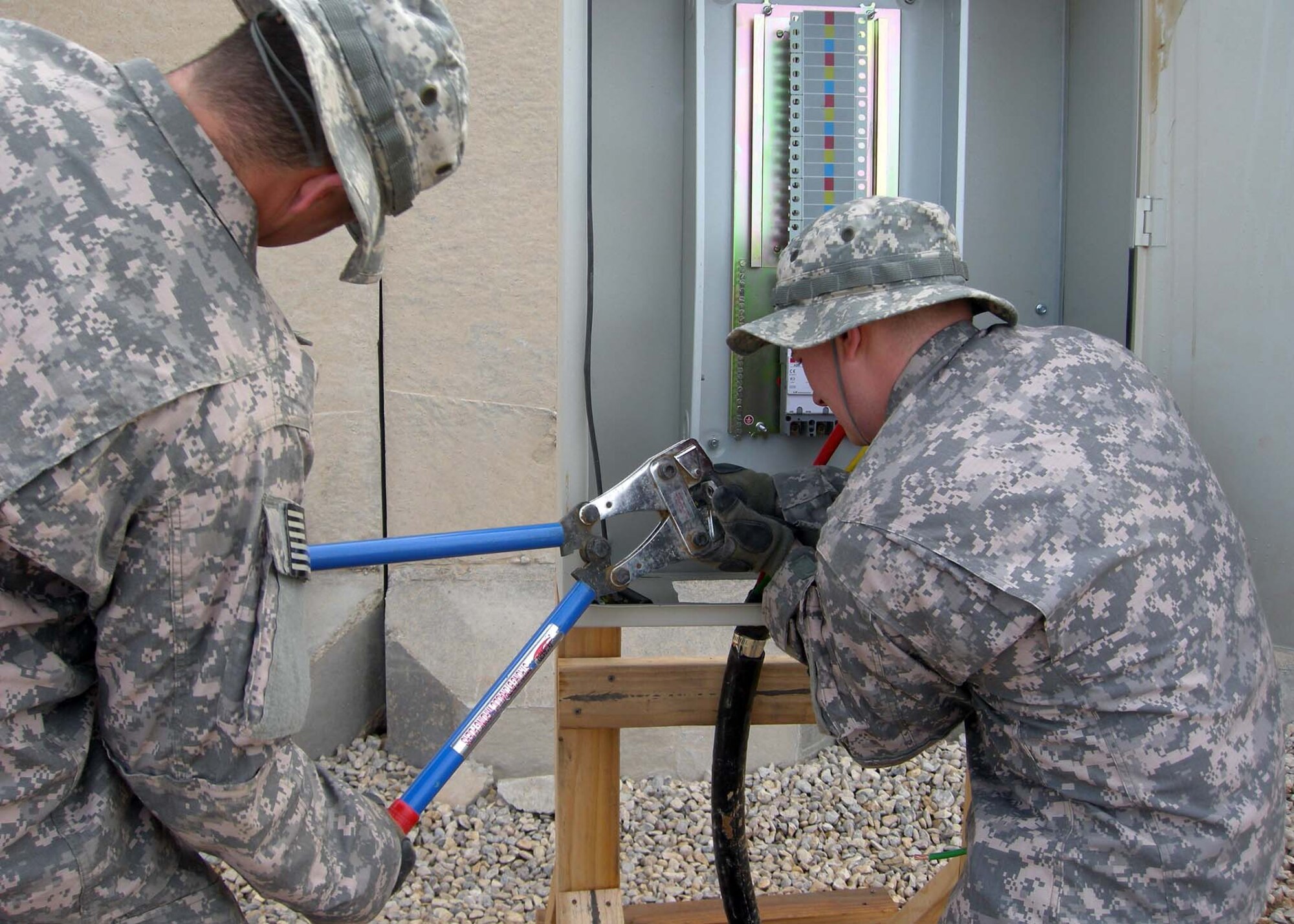 Tech. Sgt. Jason Hindmarsh and Staff Sergeant William Williams, 732nd Expeditionary Civil Engineer Squadron Detachment 3, use a cable crimper to attach a connector on an electrical line at Patrol Base Shocker, Iraq May 2009. Over 6,000 feet of electrical cable was placed to support over 15 troop billets, hygiene facilities and guard towers. The Airmen were a part of a construction team to support the vertical construction phase, which doubled the size of the installation to bed-down over 140 additional US Soldiers to be assigned to Patrol Base Shocker. Sergeant Hindmarsh and Sergeant Williams are deployed from Fairchild Air Force Base, Wash. Sergeant Hindmarsh is a native of Spokane, Wash.  Sergeant Williams is a native of Clarkston, Mich. (Courtesy Photo)