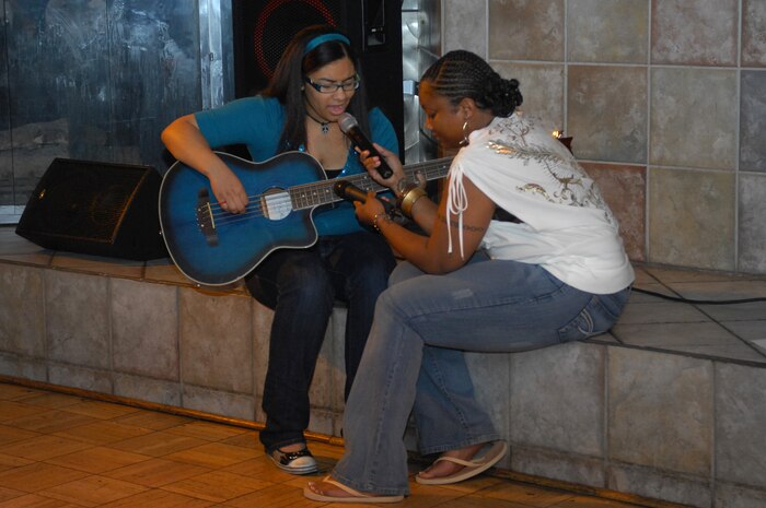 NELLIS AIR FORCE BASE, Nev. -- Tech. Sgt Dawn Brown, 99th Force Support Squadron, holds a microphone for Ms. Joselle Anderson, daughter of retired Maj. Joseph Anderson, as she performs a song she has written titled "Watermelon Seeds" during the African American Cultural Association (AACA) sponsored Open Mic Night here,  June 16.  The AACA Open Mic Night is to open to all and is held every third Tuesday of the month from 7 to 9 p.m. at the Desert Oasis Enlisted Club. (U.S. Air Force photo by Staff Sgt. Taylor Worley)