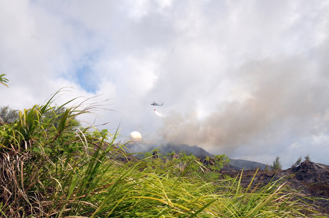 ANDERSEN AIR FORCE BASE, Guam - Aerial support from the Navy Helicopter Sea Combat Squadron 25 helps firefighters on the ground combat a brush fire climbing a ridge and threatening a Federal Aviation Administration facility. The helicopter’s bucket holds 420 gallons of water which is dumped on the fire in hard to reach areas.  Fire fighters worked from 1 to 6 p.m. before they extinguished a wild fire that burned approximately 50 acres on Mt. Santa Rosa.   (U.S. Air Force photo by Tech. Sgt. Michael Boquette)