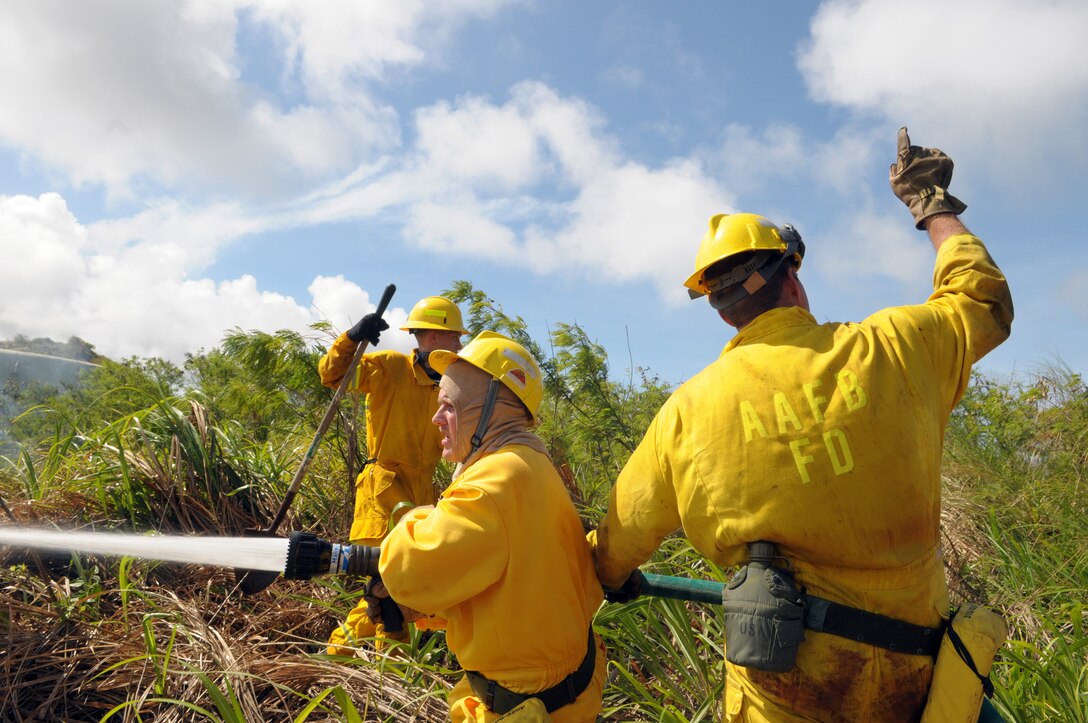 ANDERSEN AIR FORCE BASE, Guam - Staff Sgt. William Pease, 36th Civil Engineer Squadron firefighter, operates the fire hose, extinguishing an area of the fire June 17. Eric Masur, 36th CES firefighter motions back to the truck asking for more pressure while Senior Airman Kyle Houseman, 36th CES firefighter, stands ready to physically stamp out any encroaching flames. Firefighters worked from 1 to 6 p.m. to contain and extinguish a wild fire that burned approximately 50 acres on Mt. Santa Rosa.   (U.S. Air Force photo by Tech. Sgt. Michael Boquette)
