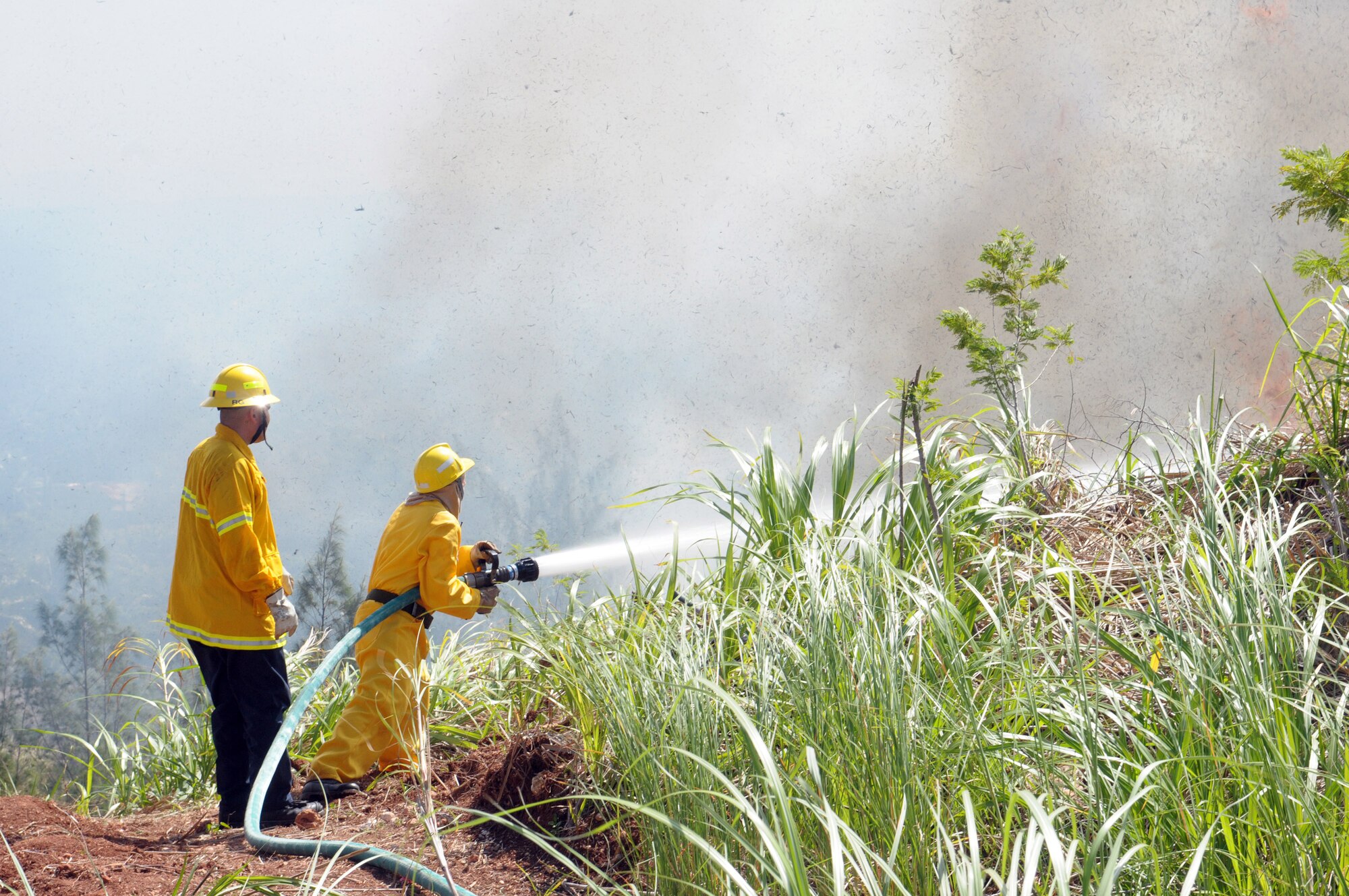 ANDERSEN AIR FORCE BASE, Guam - Ron Grajeda, 36th Civil Engineer Squadron firefighter, monitors direction of fire movement June 17. Staff Sgt. William Pease, 36th CES fire fighter, mans the fire hose and attempts to contain the advance of the fire. Firefighters worked from 1 to 6 p.m. to control and extinguish a wild fire that burned approximately 50 acres on Mt. Santa Rosa. . (U.S. Air Force photo by Tech. Sgt. Michael Boquette)