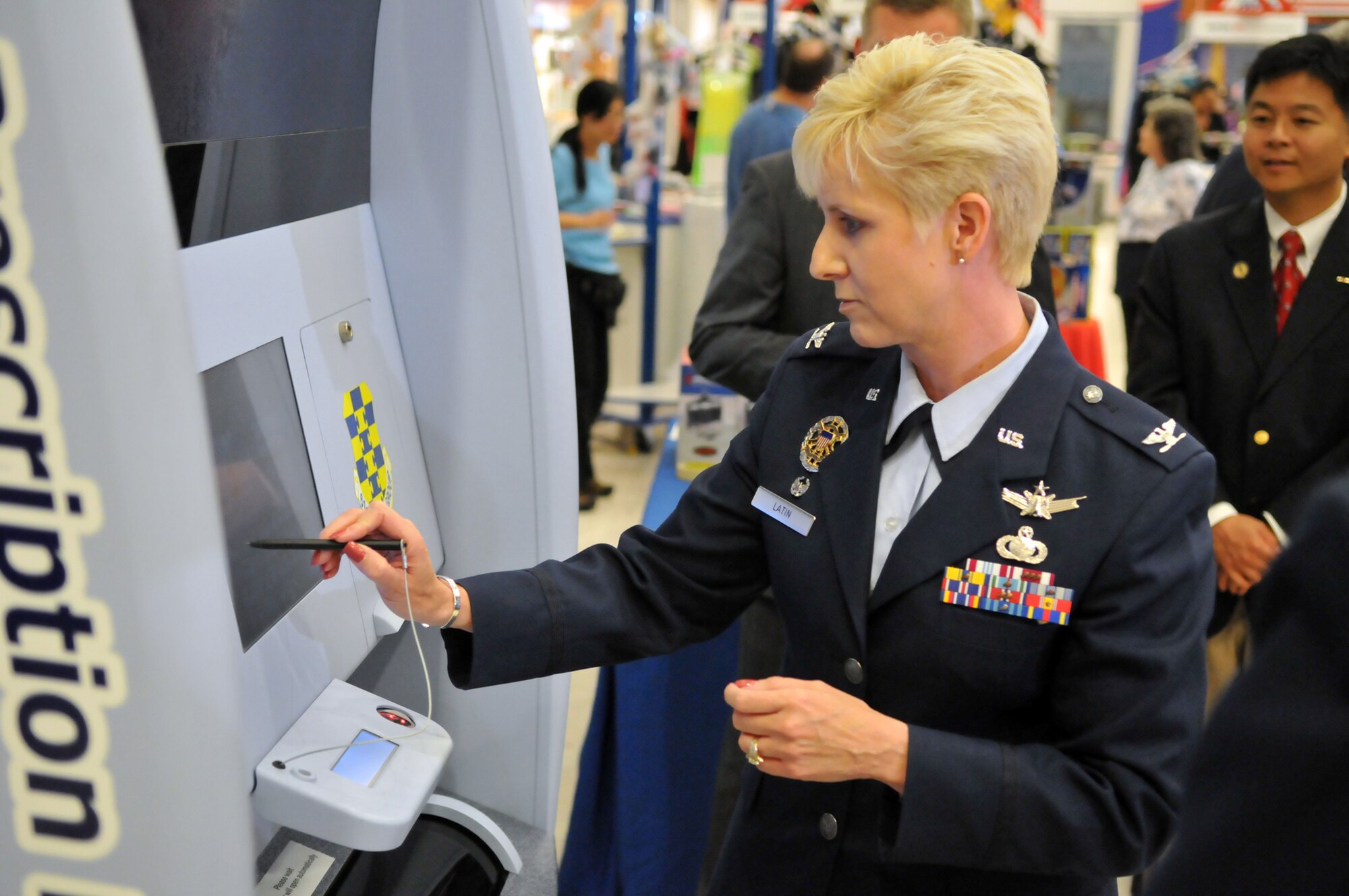 Col. Anita Latin, 61st Air base Wing commander, tries out the new automated prescription center at the ribbon cutting ceremony, June 13.  State Assemblyman Ted Lieu, pictured in the background attended the ceremony and presented a certificate of recognition to the base.    The Script Center Express Prescription Refill and Pickup Center is the first of its kind in the Air Force and DOD. (Photo by Atiba S. Copeland)