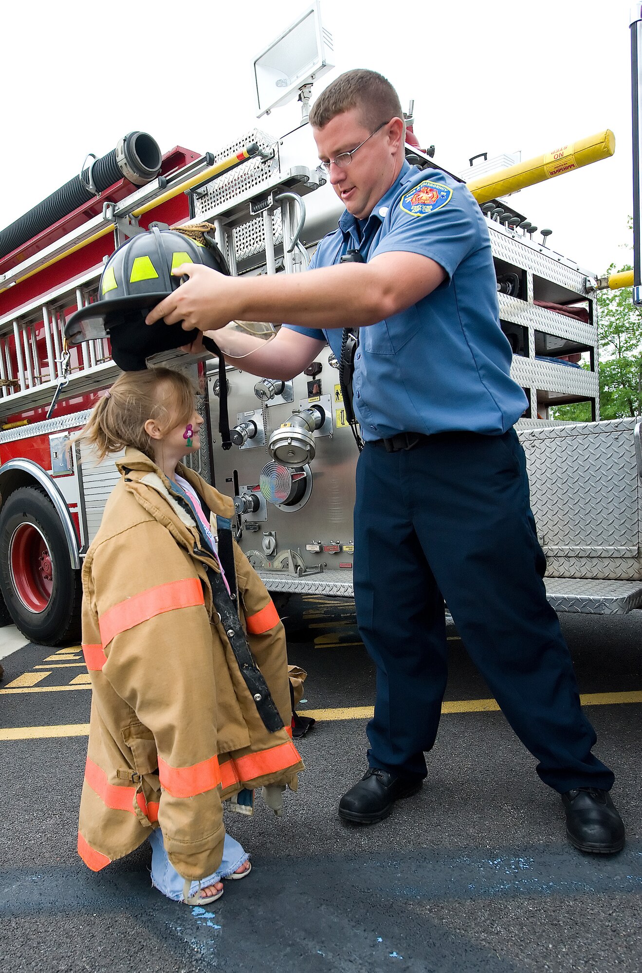 Christopher Broadwater, 436th Civil Engineer Squadron, helps CourDe' Walston, the five-year-old daughter of Staff Sgt. Nicole Walston, 436th Aerial Port Squadron, try on a firefighter coat and helmet during the Children's Mobility Line June 17.  The event was held to help children understand the process of being deployed and the equipment their parents use downrange.  (U.S. Air Force photo/Thomas Randle)