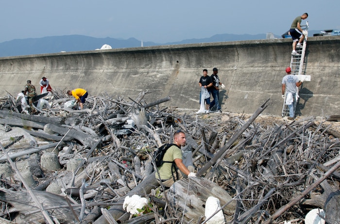 Marines and sailors from around the station rummage though rocks, branches and rotting wood to remove trash from the seawall along Penny Lake here during an Earth Day 2009 seawall cleanup June 18. Service members concentrated on removing plastics, old tires and other trash. Plans are being made to remove the rotting wood and tree branches during another cleanup.