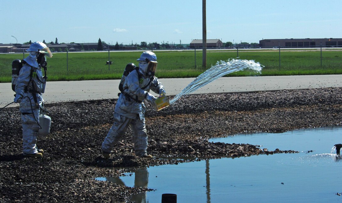(Left) Senior Airman Ryan Logan, stands by ready to ignite the fuel as Scott VanDrew, 28th Civil Engineer Squadron firefighters, throws diesel fuel into a burn pit here, June 19.  Ellsworth firefighters use pit fires to train new Airmen and Department of Defense civilian firefighters.  Pit fires are also used as refresher training for all 28th Bomb Wing firefighters. (U.S. Air Force photo/Senior Airman Anthony Sanchelli)