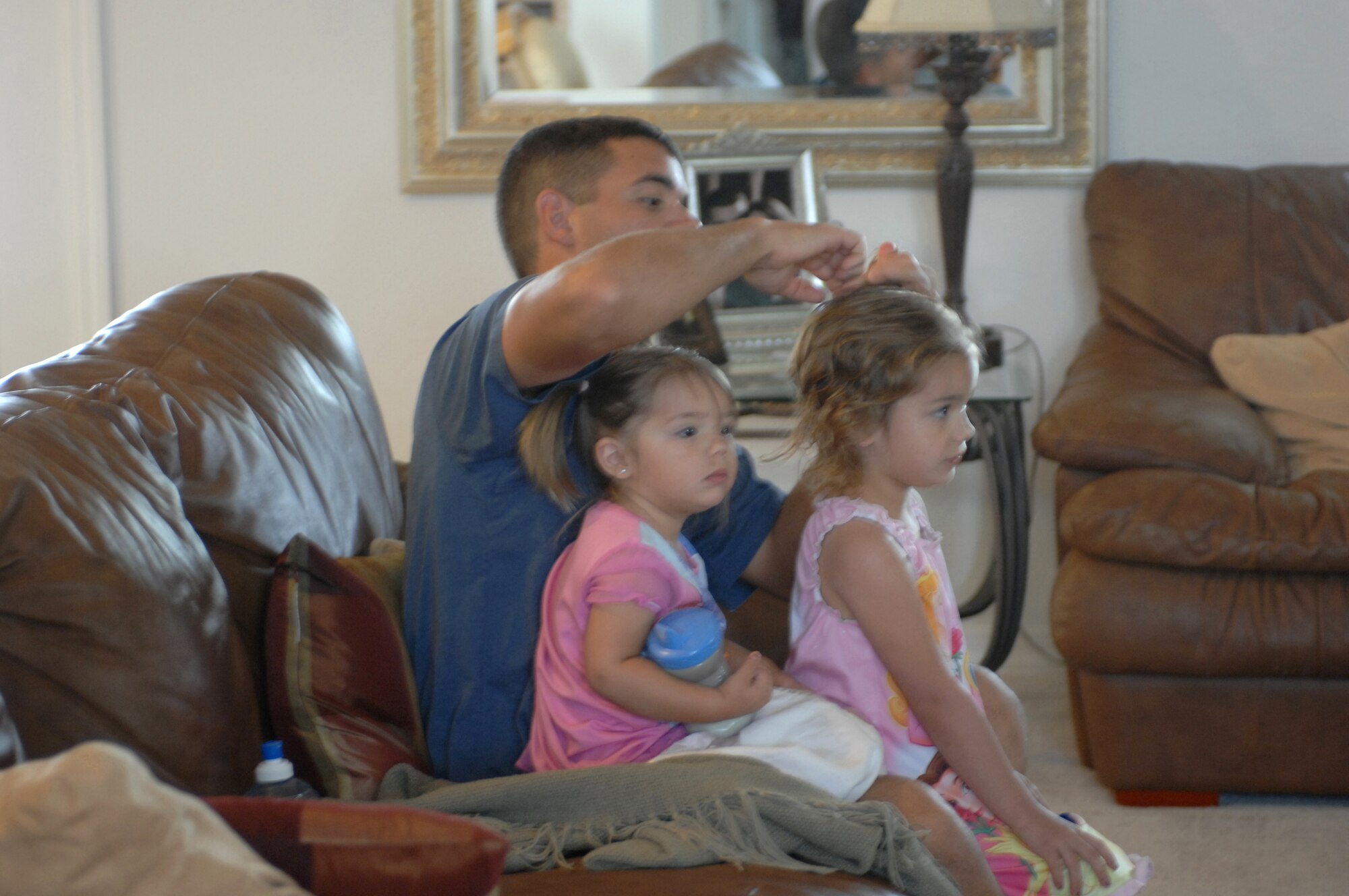 NELLIS AIR FORCE BASE, Nev. -- Clinton Collins, husband of 1st Lt. Christine Collins, a trauma nurse deployed to Bagram Air Field, Afghanistan, styles pigtails for his four-year-old daughter, Taylor. His two-year-old daughter, Reagan, enjoys morning cartoons after her hair has been put up by her dad. Mr. Collins represents a handful of dependent fathers who become the primary caretakers when their wives deploy. (courtesy photo)