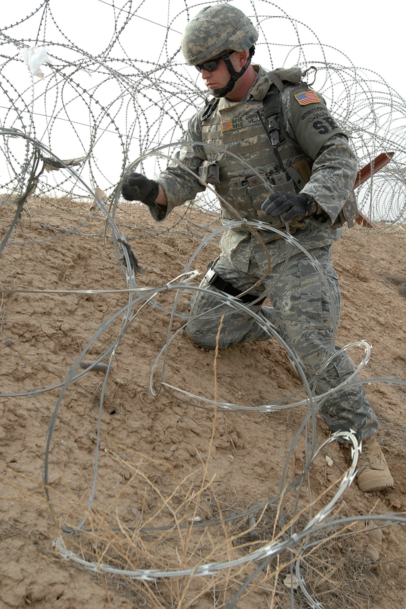 Staff Sgt. Charles Shipman, 506th Expeditionary Security Forces Squadron physical security, re-positions razor wire on a dirt berm outside the entry control point near a base gate June 12. The security measures along the approach to the ECP were redesigned to enhance base security and further facilitate safe access control of vehicles and pedestrians. The higher berm will enhance the defense-in-depth, better protecting Coalition Forces that use the ECP. Sergeant Shipman, a Savannah, Ga., native, is deployed from the 315th Airlift Wing, Charleston Air Force Base, S.C. (U.S. Air Force photo / Staff Sgt. Eunique Stevens)
