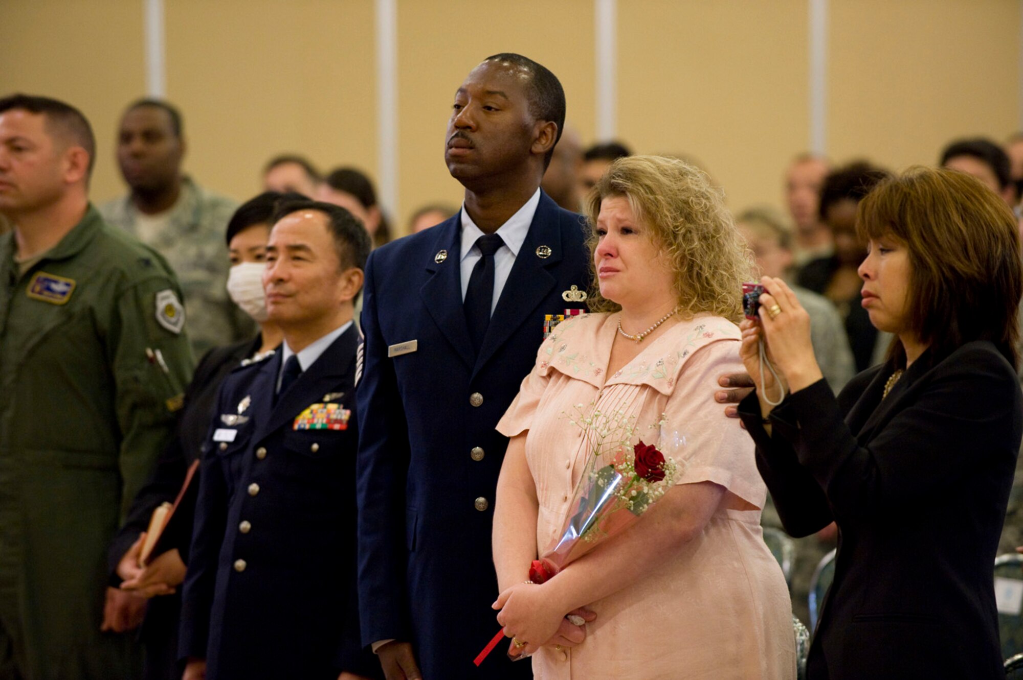MISAWA AIR BASE, Japan -- While holding a single rose, Joan Price, Chief Master Sgt. Ricky Price's wife, stands with the audience during the conclusion of her husband's retirement ceremony June 19, 2009. Mrs. Price instituted a coupon savers program, which saved an average of $1,500 a month for the Misawa Air Base community. (U.S. Air Force photo by Staff Sgt. Samuel Morse)