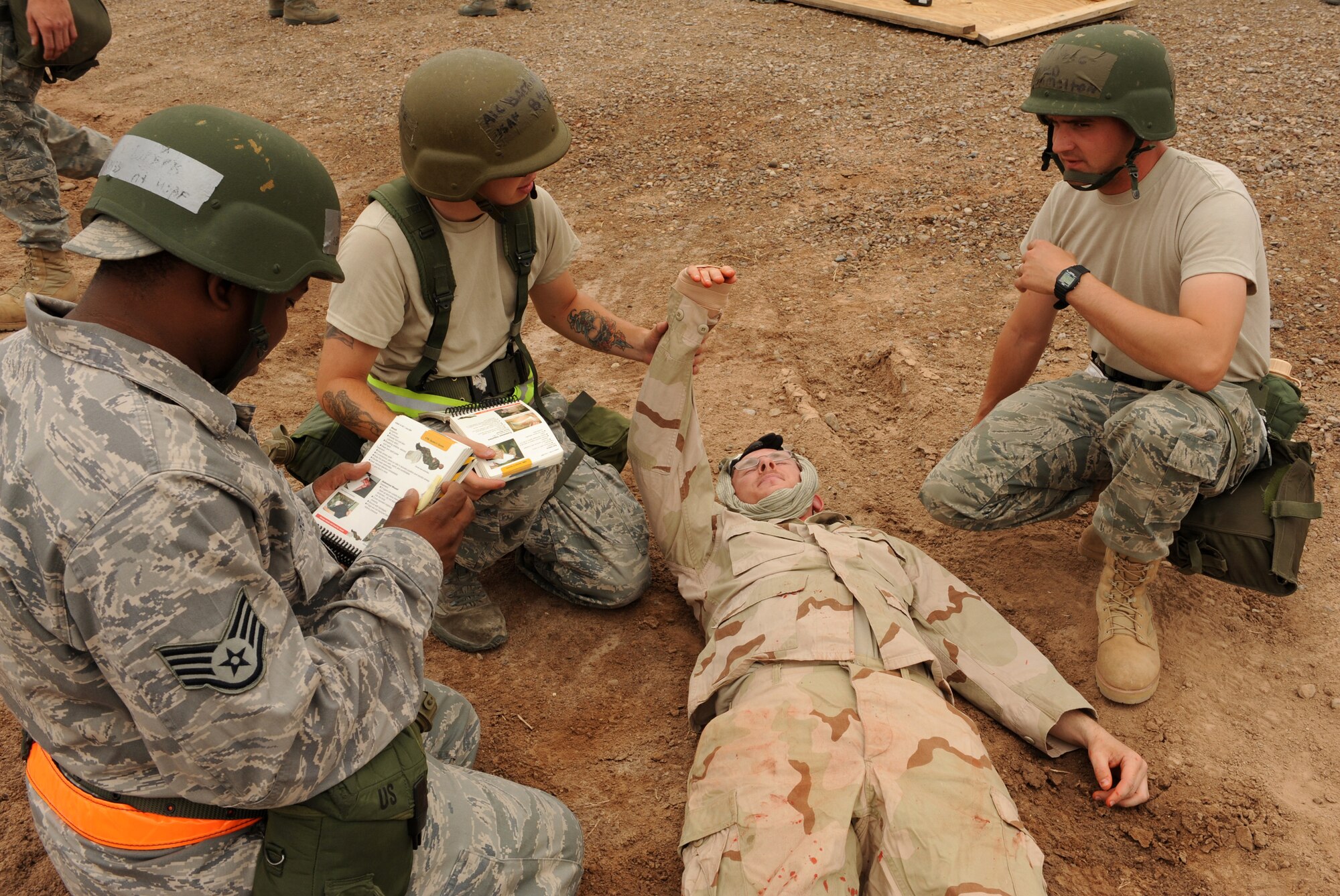 Airmen from the 49th Materiel Maintenance Squadron perform self-aid and buddy care on a simulated casualty who suffered head trauma and blood loss from his right arm after an attack on Basic Expeditionary Airfield Resources Base, June 18, at Holloman Air Force Base, N.M. One Airmen keeps the causality?s arm elevated to prevent blood loss while another uses his Airman?s Manual to find out what to do next during the Phase II exercise. (U.S. Air Force photo/Airman 1st Class Sondra Escutia)
