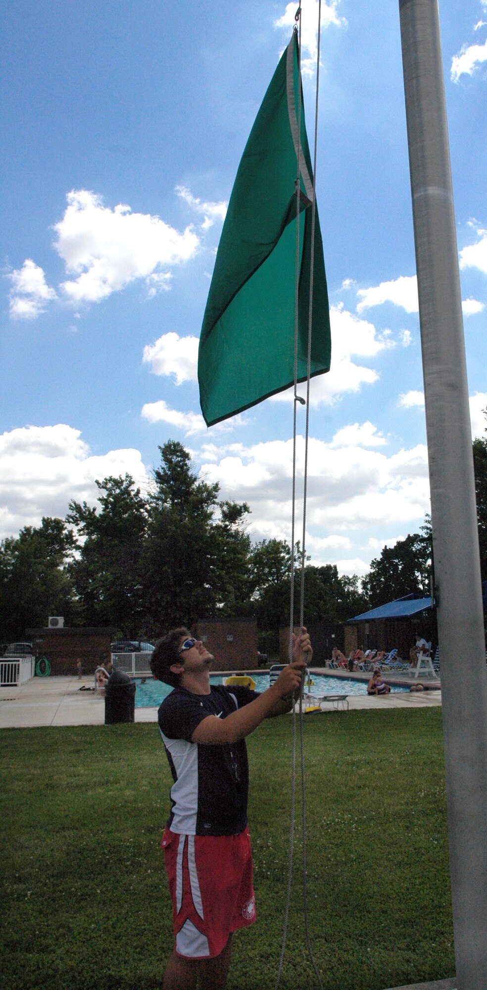 Justin Firaben, base lifeguard, raises a green flag June 23 at the pool on Bolling Air Force Base, D.C. The colored flag corresponds to the current wet bulb globe thermometer reading. A WBGT is an instrument that takes into account air movement, humidity, temperature and heat exchange, and produces a composite temperature. This composite temperature is used to estimate potential heat stress risk. (U.S. Air Force photo by Senior Airman R. Michael Longoria)