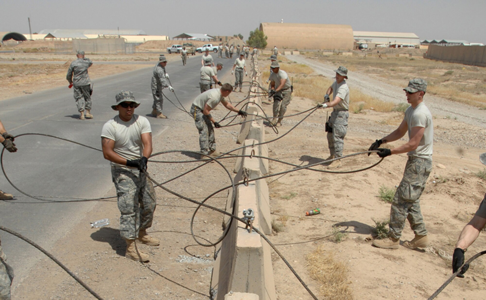 Airmen of the 506th Air Expeditionary Group thread aircraft cable through barriers to create a barricade around the Kirkuk Air Base, Iraq, flightline June 5 to mitigate vulnerabilities and lessen safety risks. The self-help security project saved an estimated $500,000 by using existing assets and volunteers. (U.S. Air Force photo/Senior Airman Eunique Stevens)
