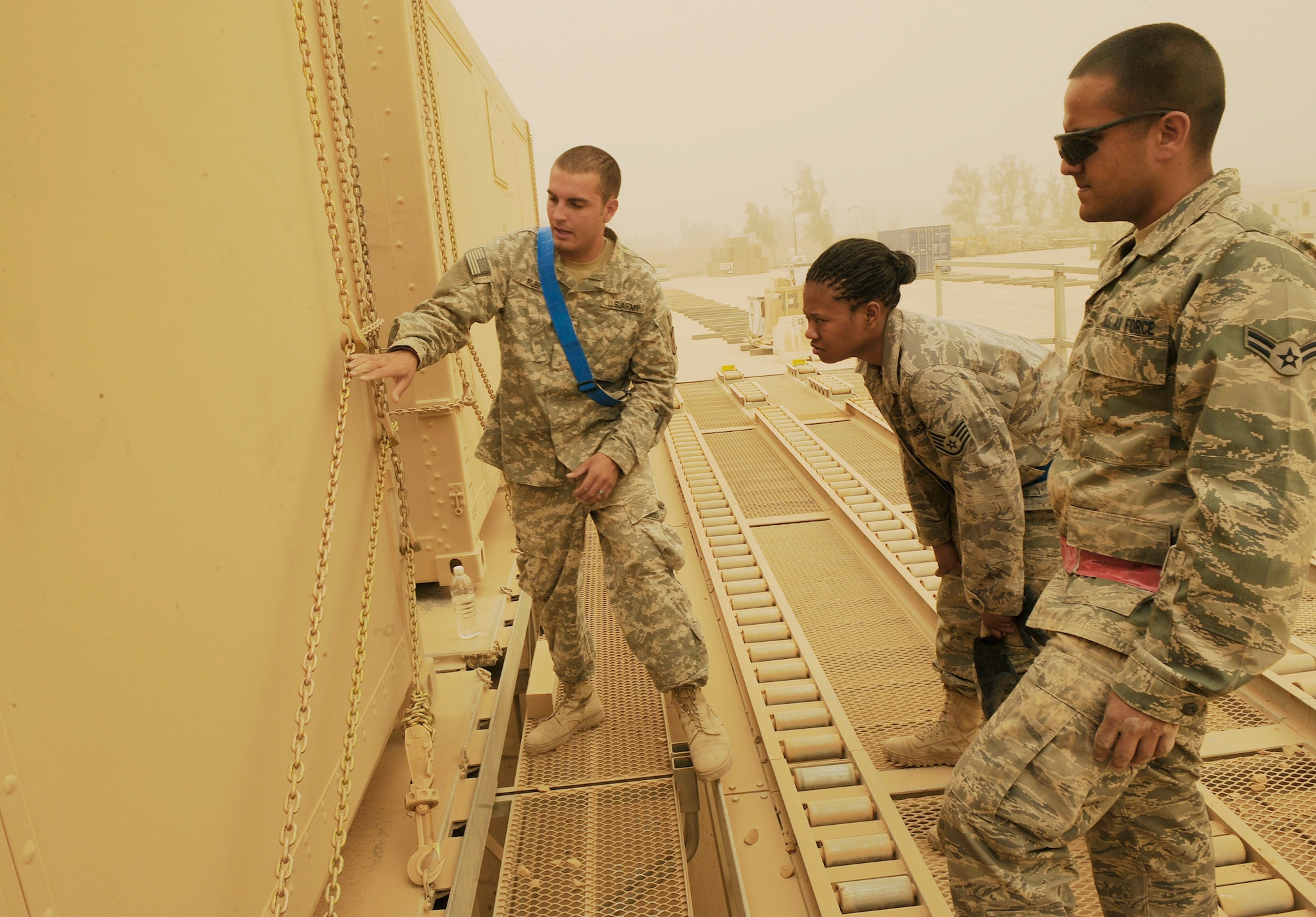 Army Sgt. Josiah Rubi shows Staff Sgt. Starlette McMillan and Airman 1st Class Manuel Babilonia how to put the chains over a metal container June 18 at Sather Air Base, Iraq. Sergeant McMillan and Airman Babilonia are part of a 16-person 22nd Movement Control Team taking over the mission from the Army?s 258th Movement Cargo Team. Sergeant Rubi is deployed from Hunter Army Airfield, Savannah, Ga. and a native of Winslow, Ariz. Sergeant McMillan is deployed from Fairchild Air Force Base, Wash., and a native of Silverdale, Wash. Airman Babilonia is deployed from Aviano Air Base, Italy, and a native of Puerto Rico. (U.S. Air Force photo/Senior Airman Jacqueline Romero)
