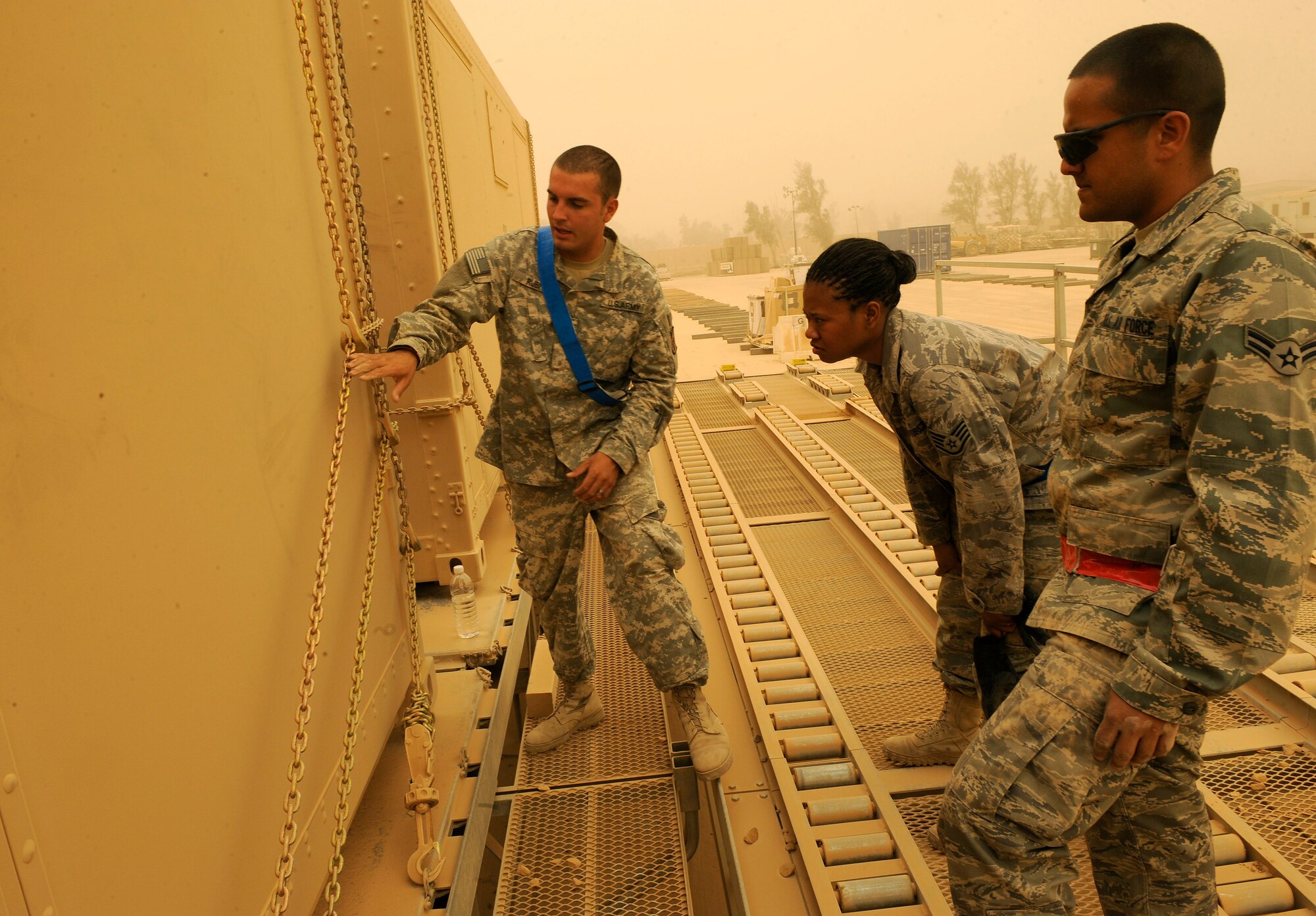 Army Sergeant Josiah Rubi, 258th Movement Cargo Team, shows Staff Sgt. Starlette McMillan and Airman 1 st Class Manuel Babilonia, 22nd Movement Control Team, how to put the chains over a metal container at Sather Air Base, Iraq June 18, 2009. Sergeant McMillan and Airman Babilonia are part of a 16-person team taking over the mission from the Army’s 258th MCT. Sergeant Rubi is deployed from Hunter Army Airfield, Savannah, Ga. and a native of Winslow, Ariz. Sergeant McMillan is deployed from Fairchild Air Force Base, Wash., and a native of Silverdale, Wash. Airman Babilonia is deployed from Aviano Air Base, Italy and a native of Puerto Rico.  (U.S. Air Force photo by: Senior Airman Jacqueline Romero)