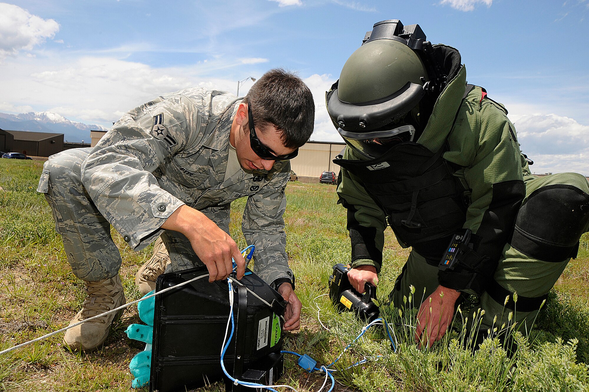 PETERSON AIR FORCE BASE, Colo.-- Airman 1st Class Achiel Pype, 21st Civil Engineer Squadron Explosive Ordnance Disposal (left), watches as Air Force Reserve Training Corps Cadet 3rd Class Benjamin Noel, wearing an EOD bomb suit designed as protective personal equipment for EOD members, sets up a real time EOD digital X-ray system in a field adjacent to Peterson's Auto Hobby Shop June 15. The system is used to investigate suspicious packages for the presence of improvised explosive devices. Peterson's EOD staff gave Cadet Noel and other cadets a small taste of what it takes to be part of an EOD team. (Air Force photo by Craig Denton)