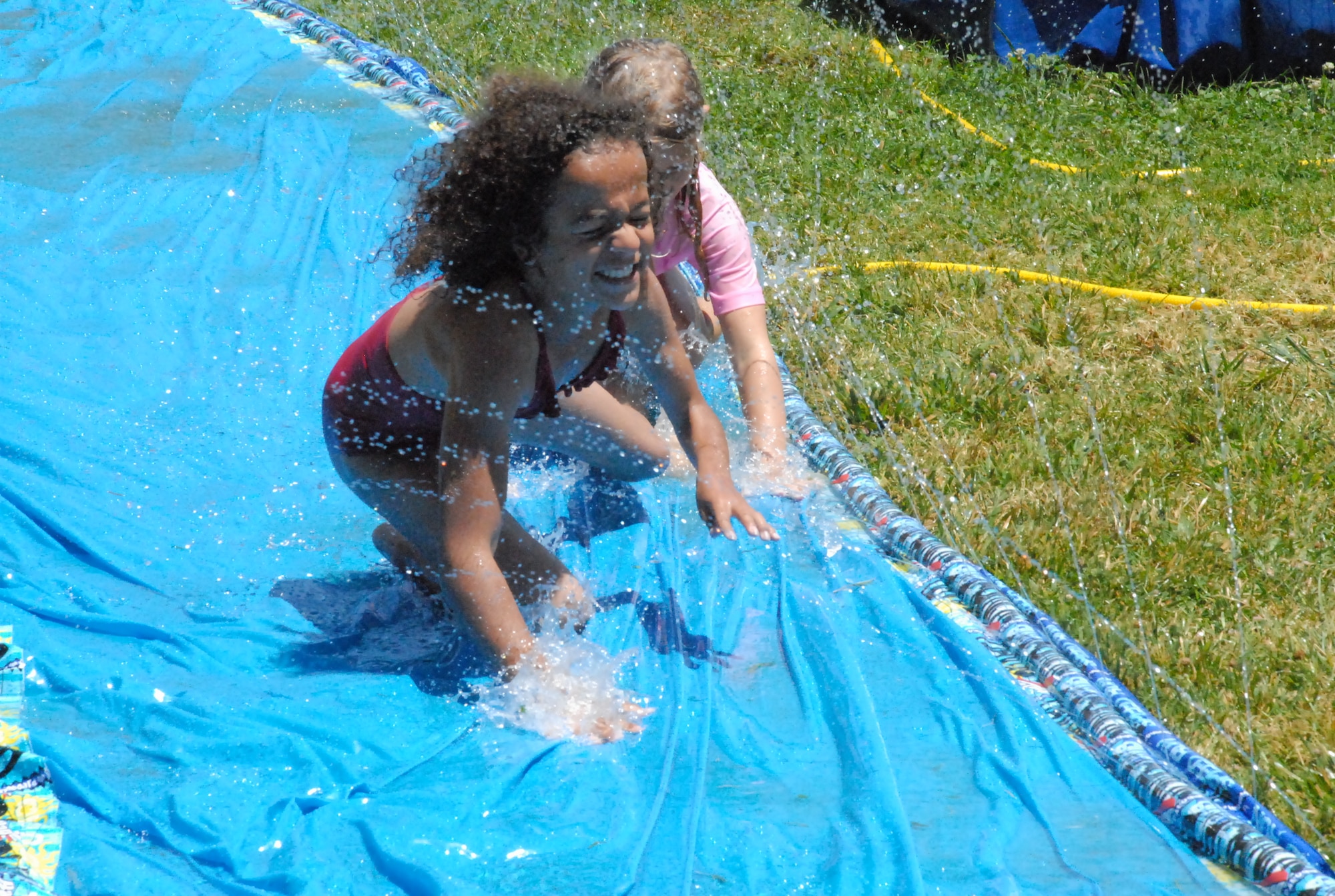 Olivia Morgan and Sydney Demallie splash down on a slip n' slide June 25 at the Youth Center. The girls were enjoying a water day as part of a recreational activity. (Photo by Airman 1st Class Chuck Broadway)
