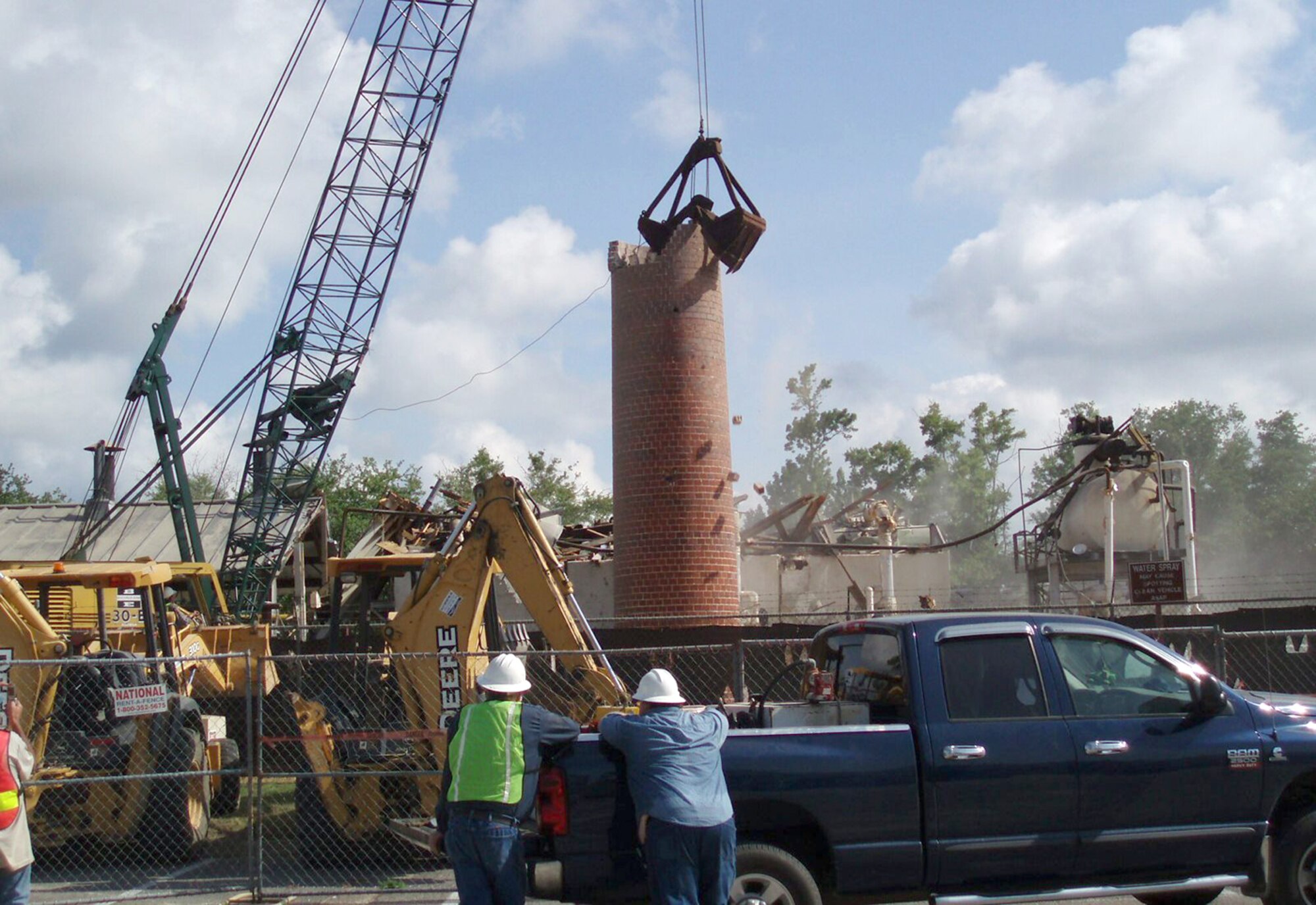 Contractors watch as the old heating plant smoke stack is reduced to rubble June 13.  Sauer Inc. workers completed demolition of the landmark, west of Keesler Medical Center, in less than 30 minutes.  The smoke stack and plant were the last vestiges of the original Keesler Field construction, circa 1941.  A parking lot will be constructed once the area is cleared.  (Courtesy photo)