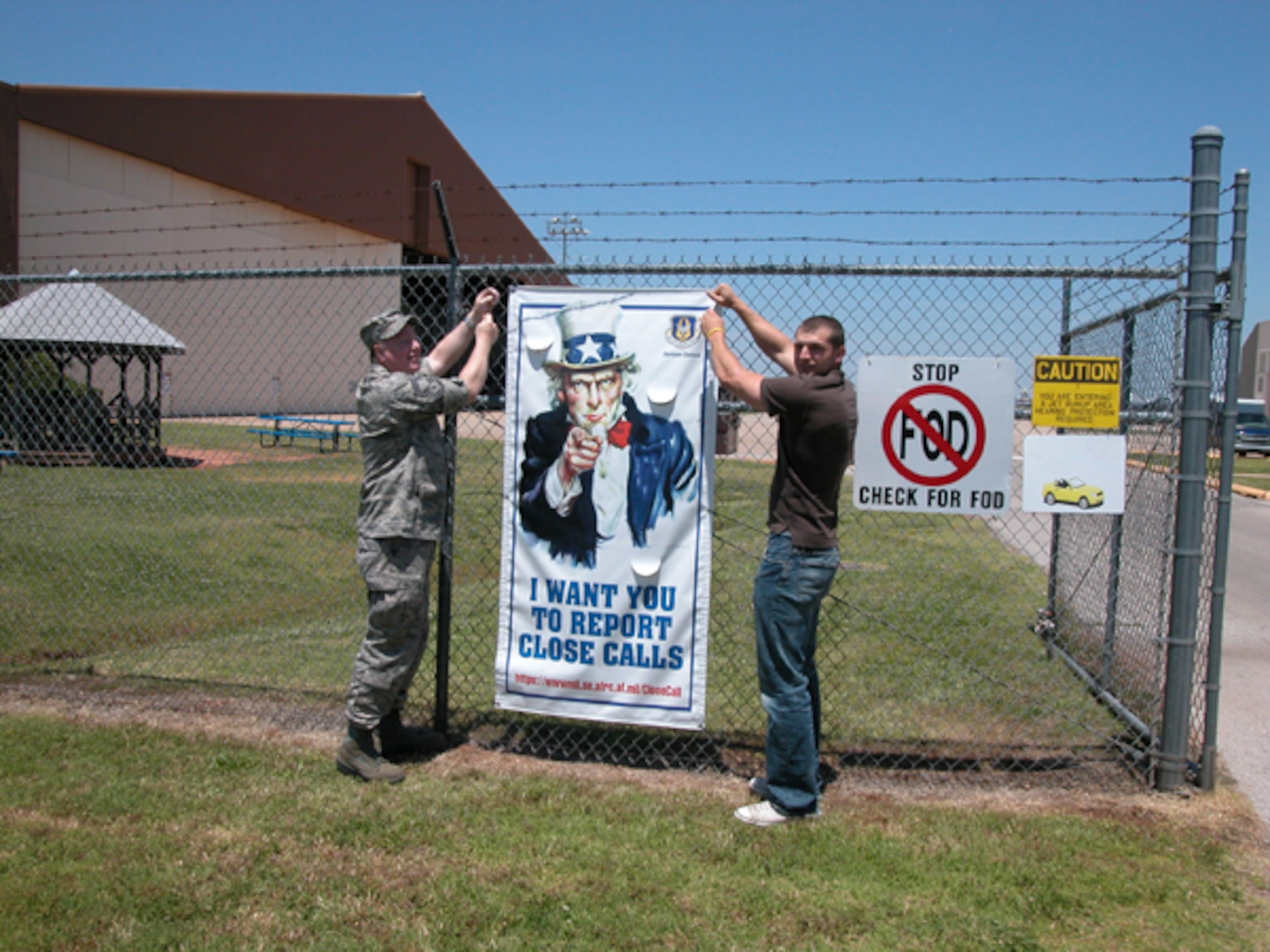 Senior Master Sgt. Gary Bristol and James Templeman from the 507 Air Refueling Wing Safety Office post a new safety poster next to the flightline entry control point.  The poster is part of a new Air Force Safety Campaign to report potential accident "Close Calls."