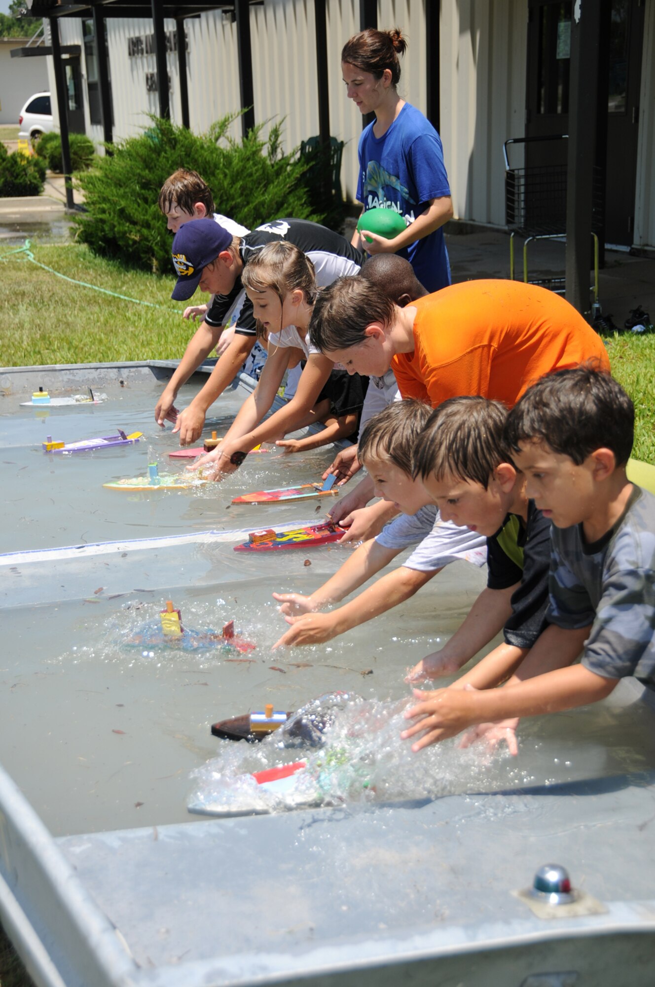 Children in last week’s woodworking camp at the arts and crafts center demonstrate their skills with a boat racing contest.  A metal boat filled with water was the race venue for the vessels built, painted and assembled by the campers and propelled by rubber band “engines.”   (U.S. Air Force photo by Kemberly Groue)