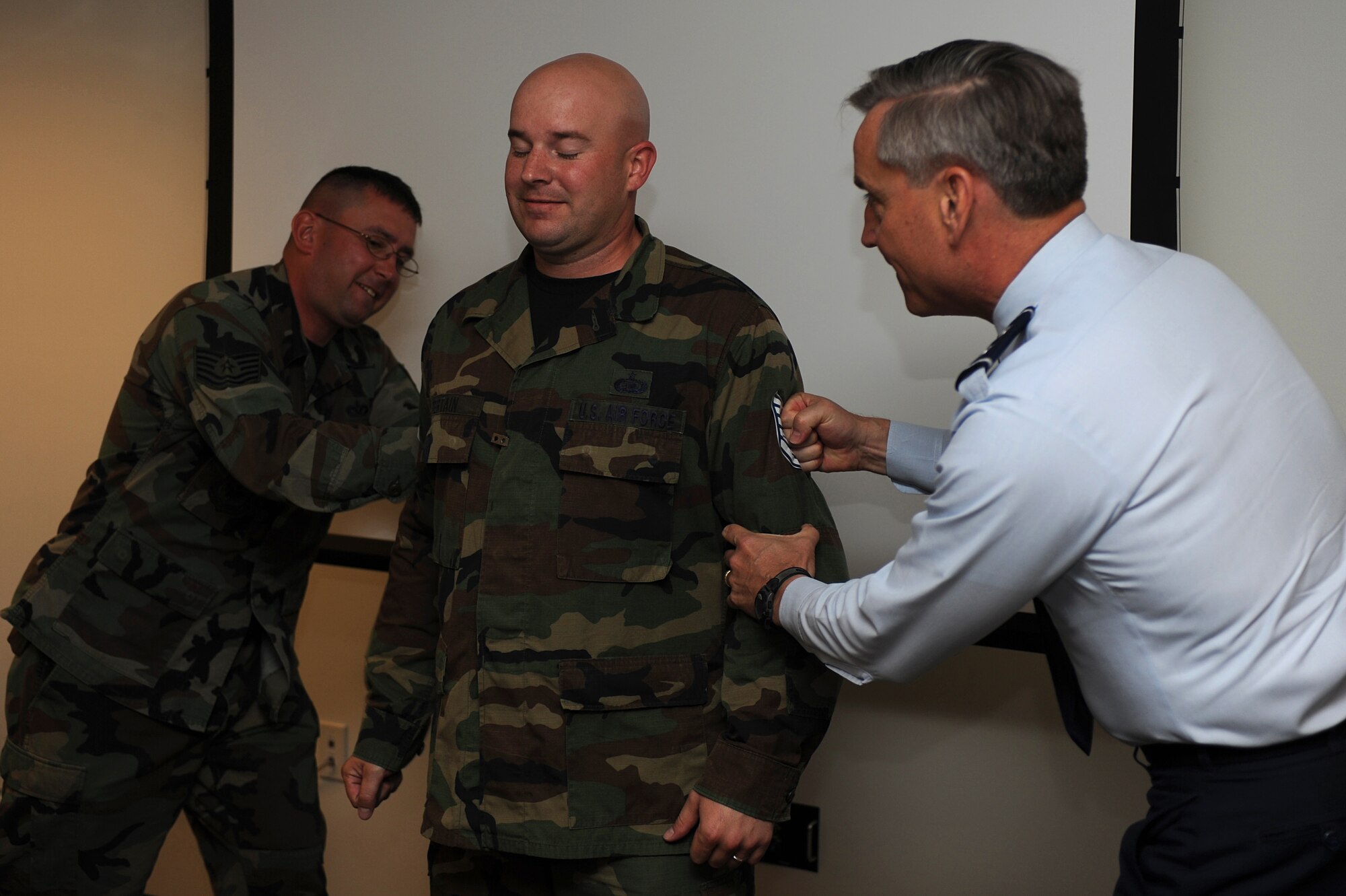 Major Gen. Kip Self (right), U.S. Air Force Expeditionary Center commander, and Tech. Sgt. Donald Satterlee, with the Expeditionary Operations School, tack technical sergeant stripes on Staff Sgt. Michael Pertain, with the 421st Combat Training Squadron, on June 18 at the center.  Twelve Airmen from the Expeditionary Center were selected for E-6 stripes. (U.S. Air Force Photo/Staff Sgt. Nathan G. Bevier) 