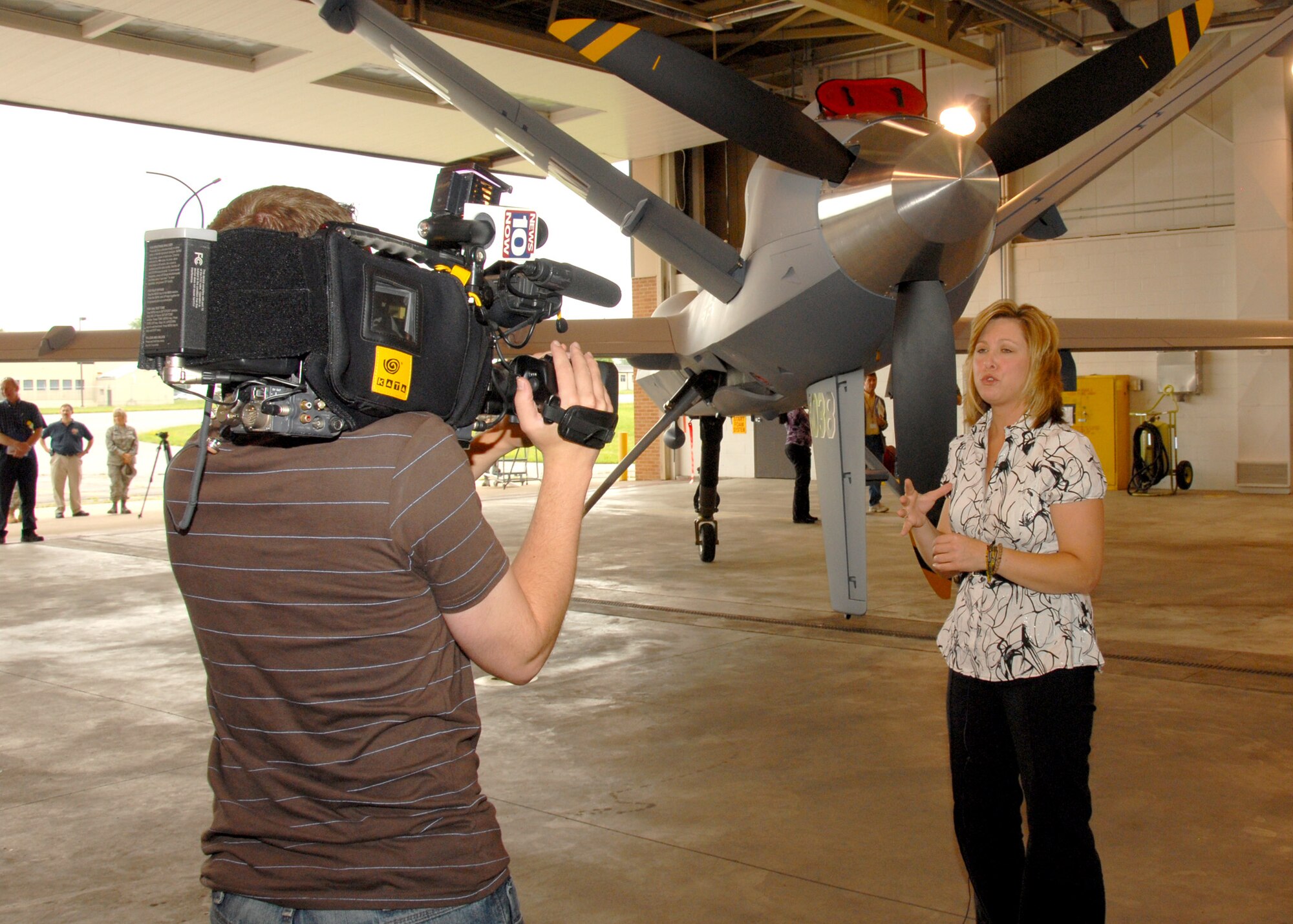 News 10 Now, Syracuse, Reporter Joleene Des Rosiers stands in front of the new MQ-9 Reaper Unmanned Aerial Vehicle while News 10 Now Operations Technician Joseph Comings records at Hancock Field in Syracuse, NY, on 26 June 2009. Des Rosiers and Comings were invited as part of the Media Day event introducing the new MQ-9 Reaper Unmanned Aerial Vehicle mission of the 174th Fighter Wing. (US Air Force photo by Tech. Sgt. Jeremy M. Call/Released)