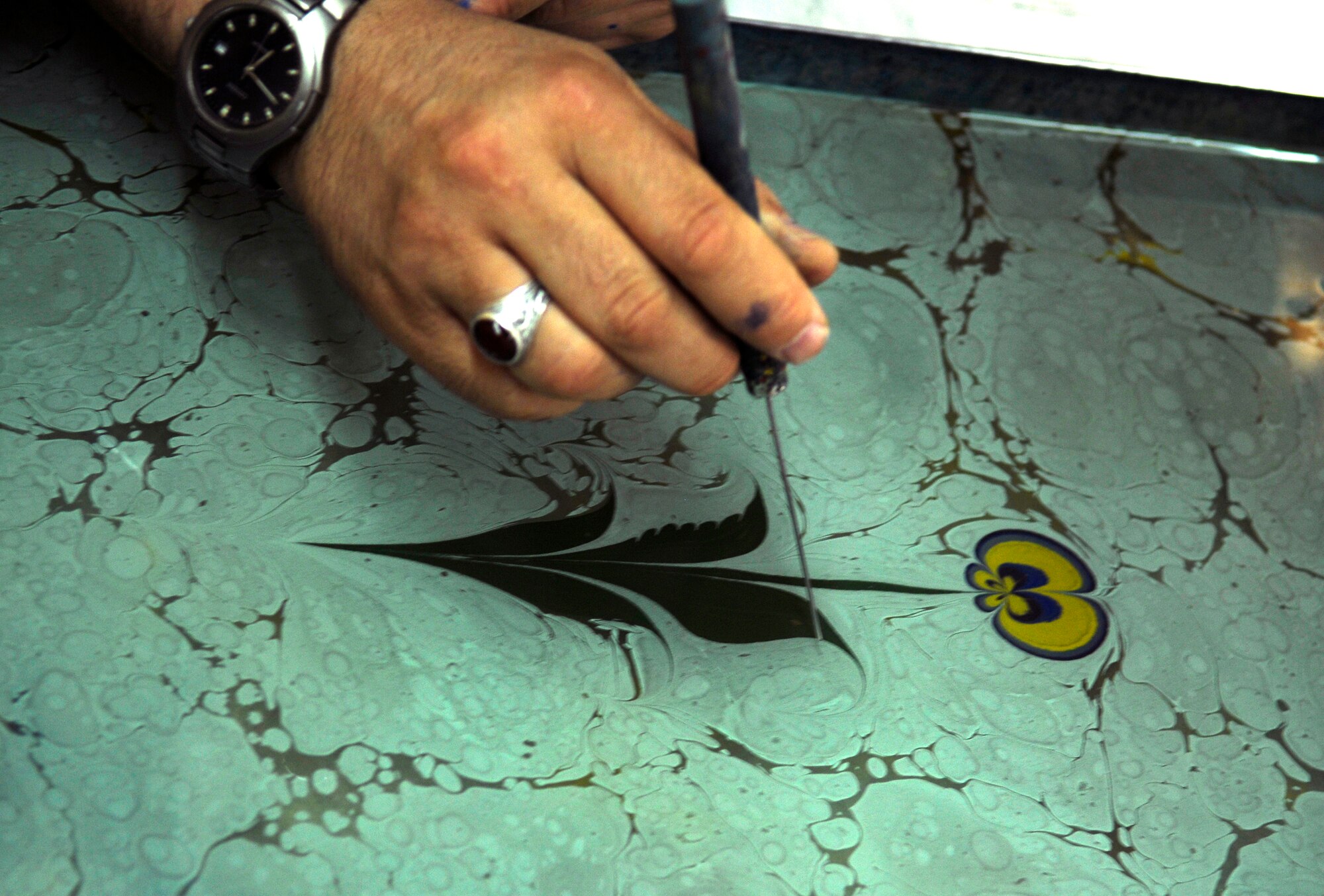 Mesut Dikel, an Ebru art instructor, demonstrates how to create a flora design during a class Wednesday, June 24, 2009 at the Arts and Crafts Center here.  Mr. Dikel has been creating Ebru art, a unique Turkish art form, for nearly 24 years.  Ebru, or paper marbling, has been practiced in Turkey since the 15th century and uses all-natural products, from the brushes to the paints.  The center plans to offer the class monthly.  (U.S. Air Force photo/Staff Sgt. Raymond Hoy)