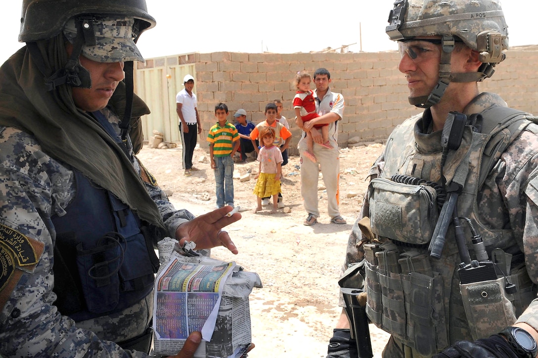 U.S. Army 1st Lt. Pete Van Hooser gives an Iraqi policeman handbills to distribute in eastern Baghdad, Iraq, June 21, 2009. Hooser is assigned to the 82nd Airborne Division's Company A, 2nd Battalion, 505th Parachute Infantry Regiment, 3rd Brigade Combat Team.