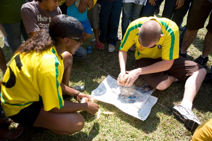 Lance Cpl. Derek Miller, an Aircraft Rescue Firefighter with Marine Wing Support Squadron 171, furiously shaves coconut meat while his teammate Cpl. Courtney A. Jones provides encouragement at a community relations event with a local Malaysian orphanage during exercise Air Warrior here June 26. The Malaysians demonstrated their gratitude to all competitors by providing them with a going away gift.