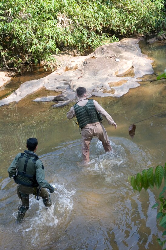 Royal Malaysian Air Force Capt. Mohd Azizi bin Musa and Marine All-Weather Fighter Attack Squadron 225 1st Lt. Steve Bradford, cross a river to begin their jungle navigation to the landing zone during a search and rescue exercise here June 28. For exercise purposes, Musa and Bradford were allowed only what they would normally parachute into the jungle with after ejecting from their respective aircraft - fortunately that included a machete.