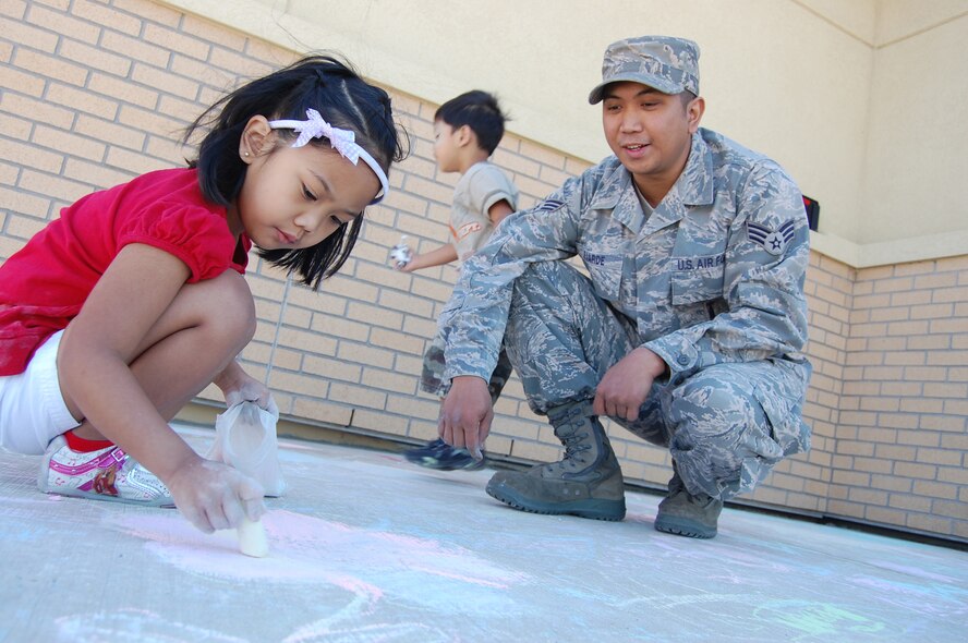 Senior Airman Abel Lejarde Jr., 341st Missile Maintenance Squadron, watches his daughter, Little Warrior Aibel, 4, works on her chalk artwork June 19 as part of the 10th Annual Chalk-It Up sidewalk art competition in the Youth Program Center parking lot. Airman Lejarde brought his dad from the Philippines as part of a summer family reunion. (U.S. Air Force photo/Staff Sgt. Marcus McDonald)