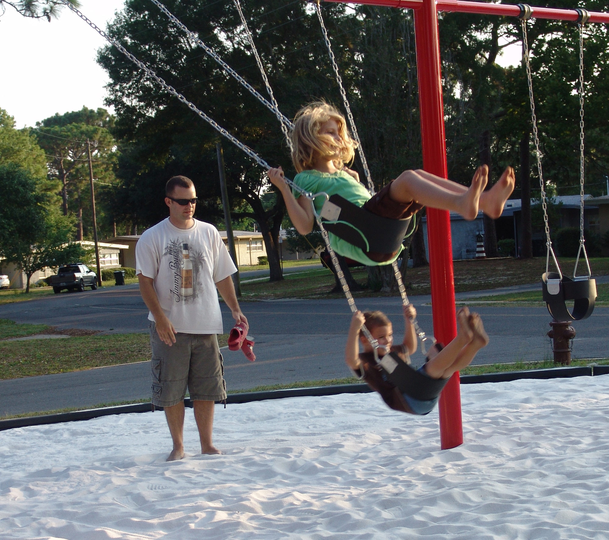 Army Capt. Corbin Copeland pushes his children Kaylee and Justin on the swings at the new playground on Chinquapin Drive.  Three new playgrounds are now open for children living in base housing. (USAF photo/Lois Walsh)                        