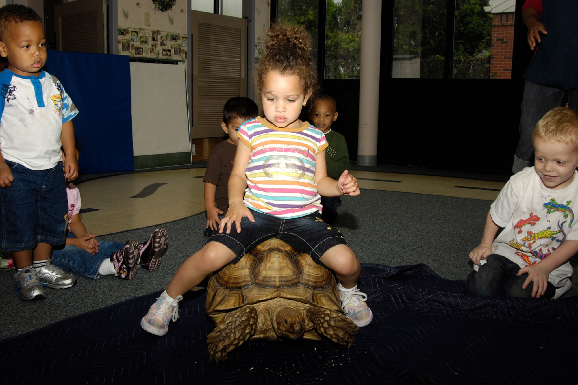HANSCOM AIR FORCE BASE, Mass. – Keara Hayes gets a ride on a tortoise while, Brendan Cochrane (left), and Anthony Legrow (right) look on. Children had the opportunity to interact with and learn about mammals, amphibians, reptiles and arachnids during the Curious Creatures visit to the center on June 25. (U.S. Air Force photo by Linda LaBonte Britt)