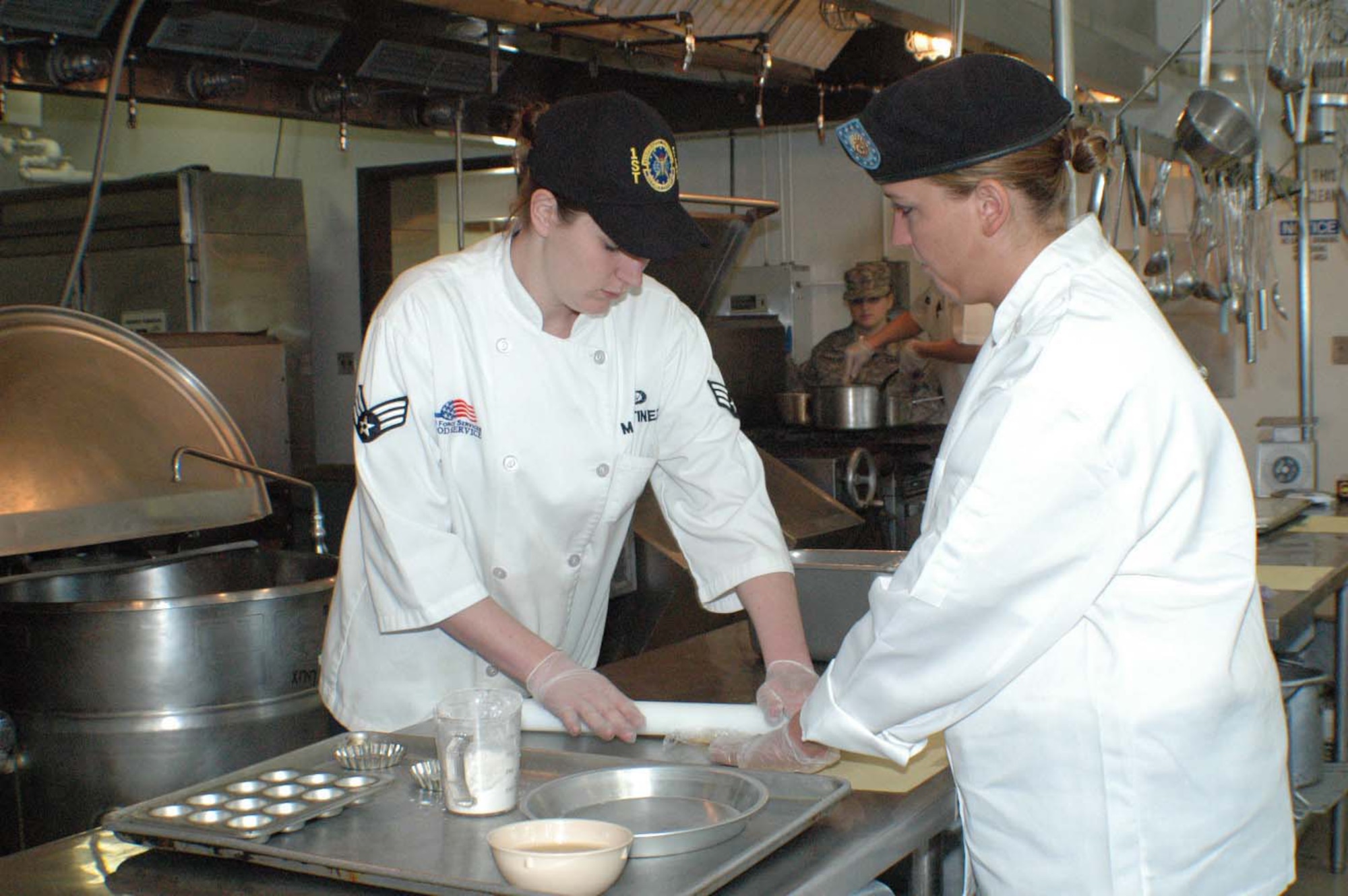 LANGLEY AIR FORCE BASE, Va. -- Senior Airman Ashley Martinez, 1st Force Support Squadron demonstrates a technique for rolling pie dough to Army Pfc. Trisha Janes from Fort Eustis. (Courtsey photo/Lyna Tucker)
