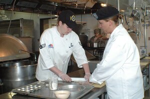 LANGLEY AIR FORCE BASE, Va. -- Senior Airman Ashley Martinez, 1st Force Support Squadron demonstrates a technique for rolling pie dough to Army Pfc. Trisha Janes from Fort Eustis. (Courtsey photo/Lyna Tucker)