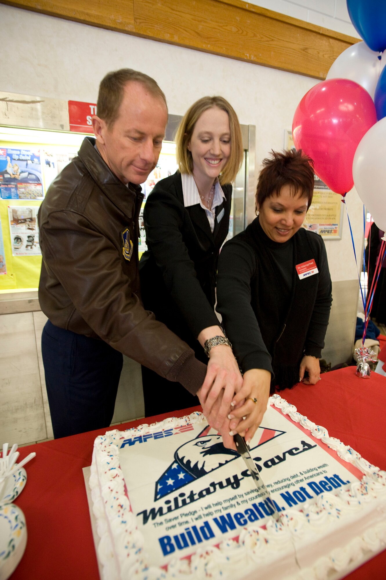 MISAWA AIR BASE, Japan -- From left to right, Col. David Stilwell, 35th Fighter Wing commander, Deanna Dlugeiwicz, Airman and Family Readiness Center community readiness technician, and Rita Inchaurregui-Powell, AAFES sales and merchandise manager, make the ceremonious first cut into a cake March 2, 2009. The cake celebrated the kick off of Military Saves Week at Misawa Air Base. (U.S. Air Force photo by Staff Sgt. Samuel Morse)