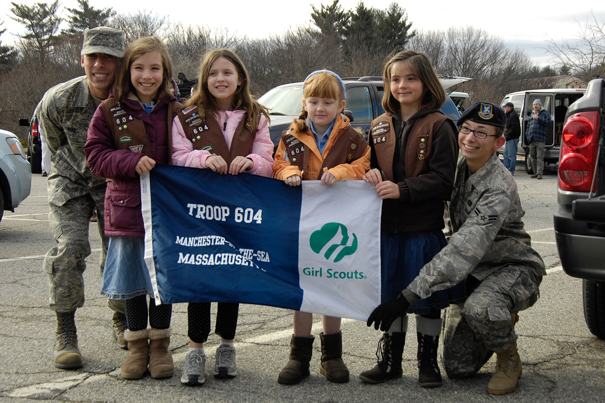HANSCOM AIR FORCE BASE, Mass. - Airman First Class Richard Ruiz (left) and Airman First Class Christine Bernard (right) have their photo taken with Girl Scouts from Troop 604 in Manchester by the Sea, Mass., after helping the girls to unload the cases of cookies that they delivered to the base on Feb. 28. Girl Scout troops from across Eastern Mass. participated in Operation Cookie Drop delivering more than 15,000 boxes of cookies to send to deployed military personnel. The girls had the opportunity to talk to and have their photos taken with Airmen, Soldiers, Sailors and Marines. (U.S. Air Force photo by Linda LaBonte Britt)