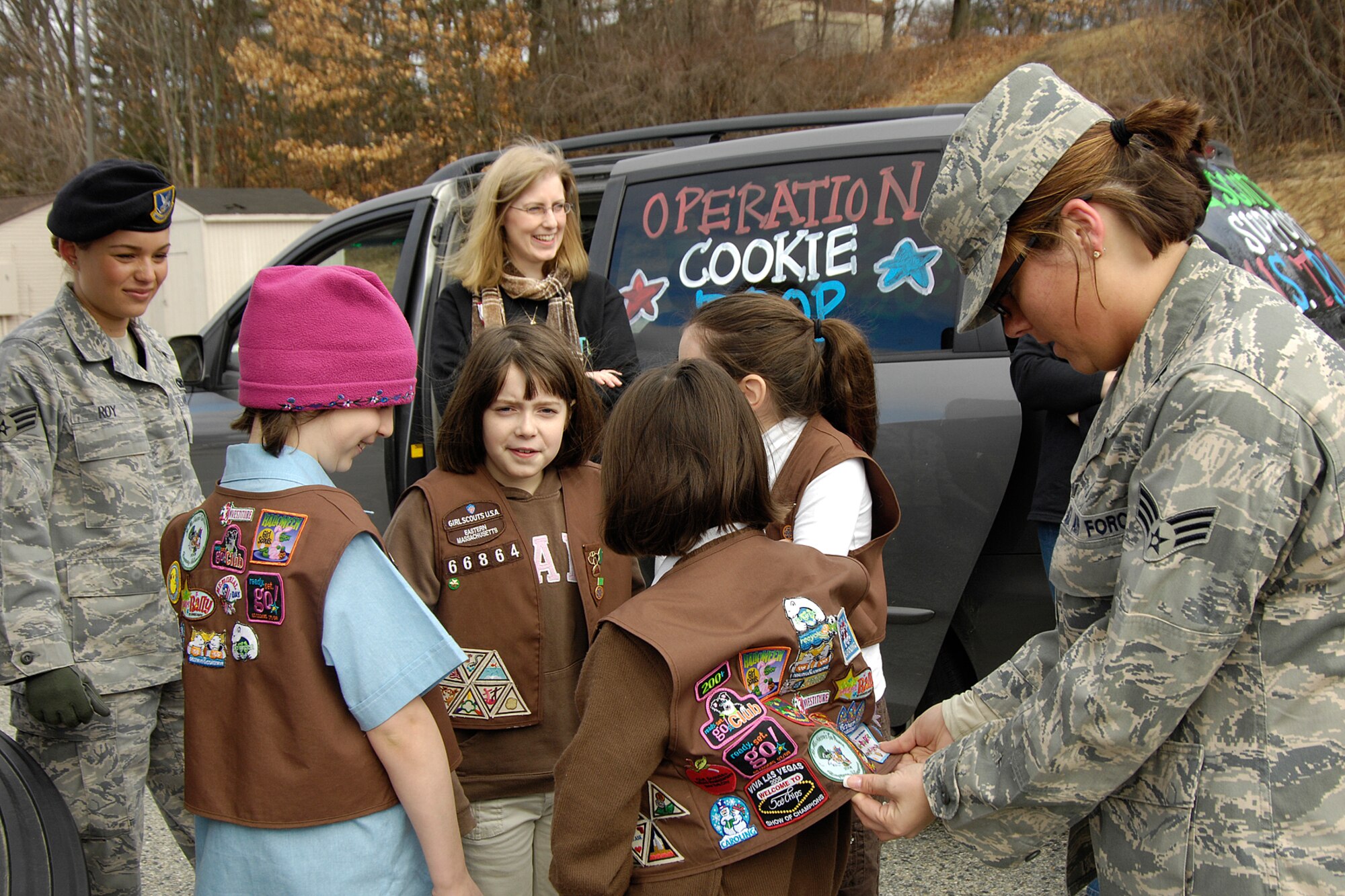 HANSCOM AIR FORCE BASE, Mass. – Senior Airman Megan Stanton (right) and Senior Airman Haley Roy (left) look at Girl Scout merit badges during Operation Cookie Drop on Feb. 28. Approximately 1,000 Girl Scouts of Eastern Massachusetts, parents and troop leaders visited Hanscom to deliver 15,000 boxes of Girl Scout cookies that the scouts collected for deployed personnel. In addition to the cookies, 2,000 pounds of coffee was delivered for overseas military personnel. Several local troop care package drive organizations were on hand to pick up the cookies and coffee to send to military personnel at deployed locations. (U.S. Air Force photo by Linda LaBonte Britt)