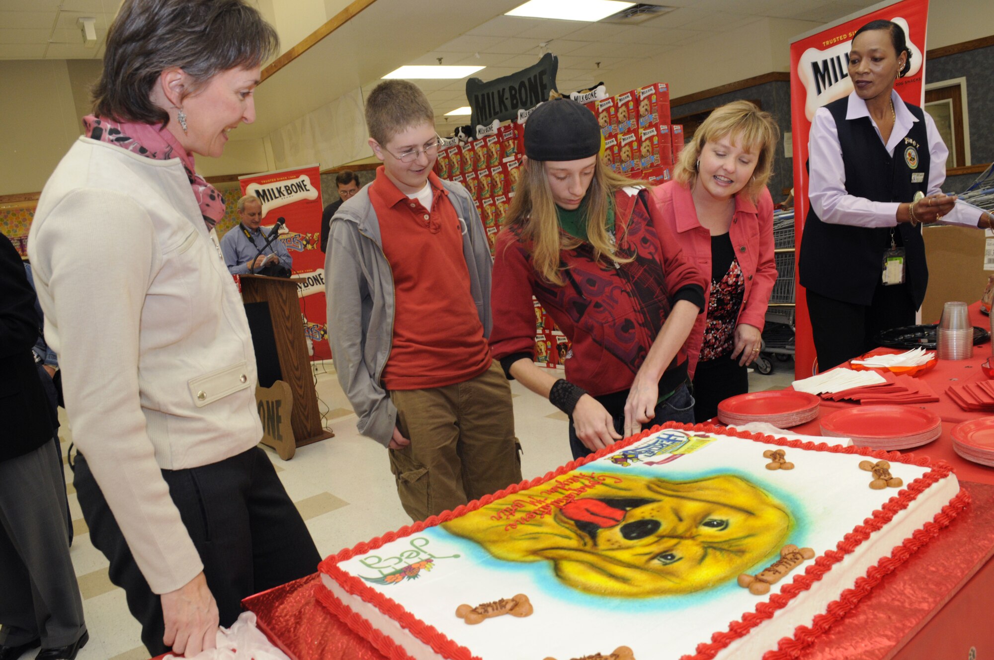 Hayden Martin, center, cuts a cake in his honor at a ceremony at Robins Commissary Feb. 26 as Marie Berry, Connor Martin, Dede Martin and Paula Lewis look on.  Hayden will be getting his own service dog through a partnership between Milk-Bone and the Defense Commissary Agency. U. S. Air Force photo by Sue Sapp