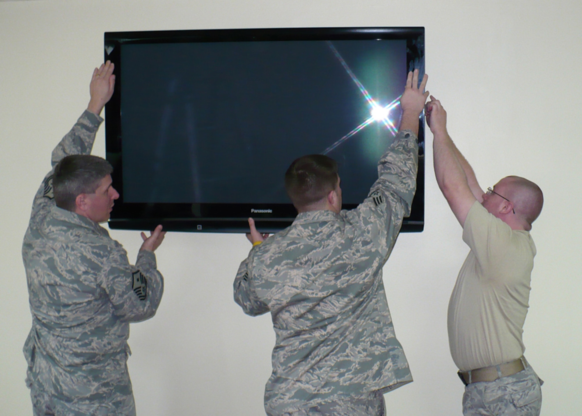 KADENA AIR BASE, Japan -- Master Sgt. Michael Frazier (left), 353rd Maintenance Squadron first sergeant, Senior Airman Brian Schutz (center), 353rd MXS, and Airman 1st Class Joshua Savage, 353rd Operations Support Squadron, hang a flat-screen television on the wall in the third floor dayroom of dormitory 758 here.  The dorm residents', who are predominately 353rd Special Operations Group and 18th Medical Group Airmen, won the base's last Dorm of the Quarter Award and the $2,000 that goes along with it. Before winning the competition, the residents were busy with several improvement projects that included the day rooms on the first three floors, and are in the process of renovating the fourth floor dayroom. (Courtesy photo)